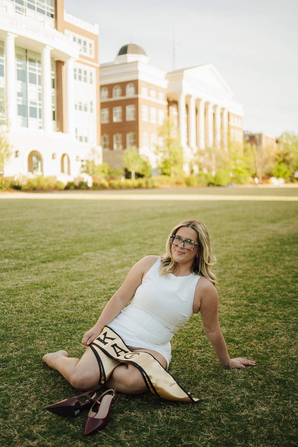 a college senior in a while sitting in the grass during her grad photo session.