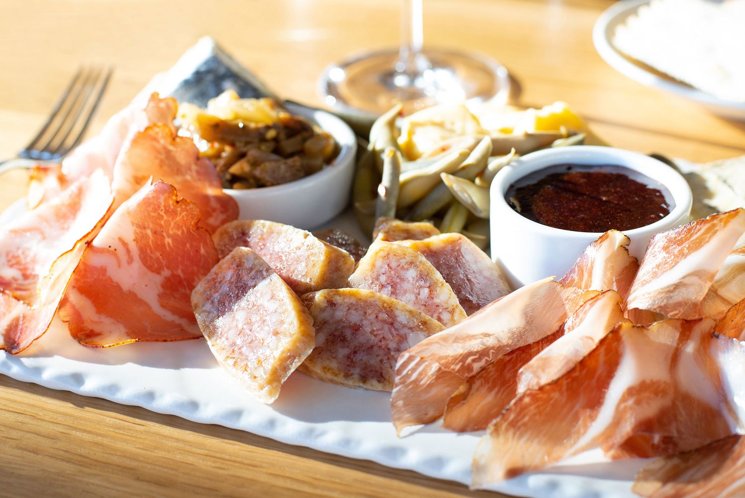 Charcuterie plate with cured meats, pâté, mustard, olives, and dipping sauces on a wooden table.