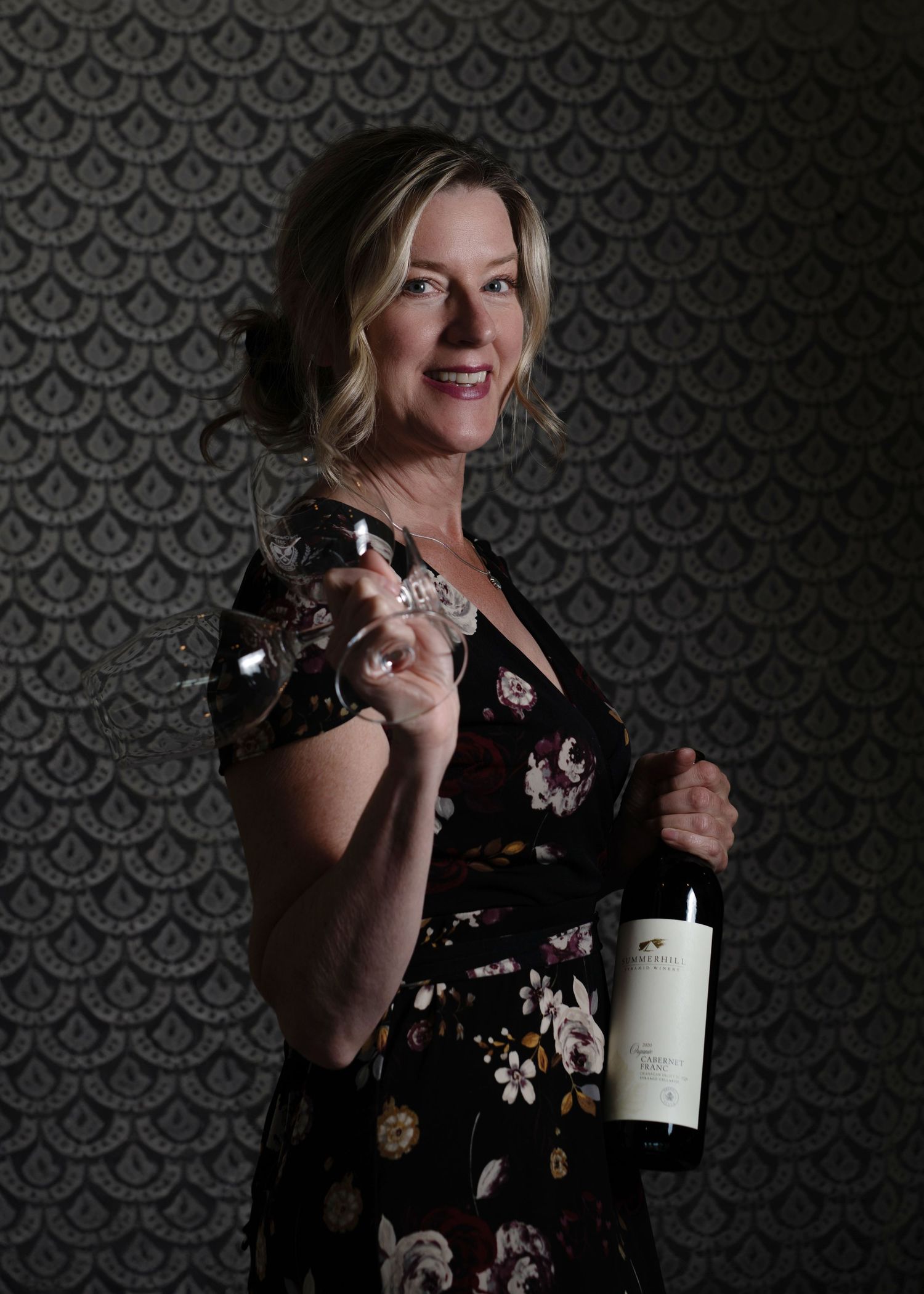Self-portrait of Tania Veitch holding two wine glasses and Summerhill wine bottle against lace backdrop, Okanagan brand photo.