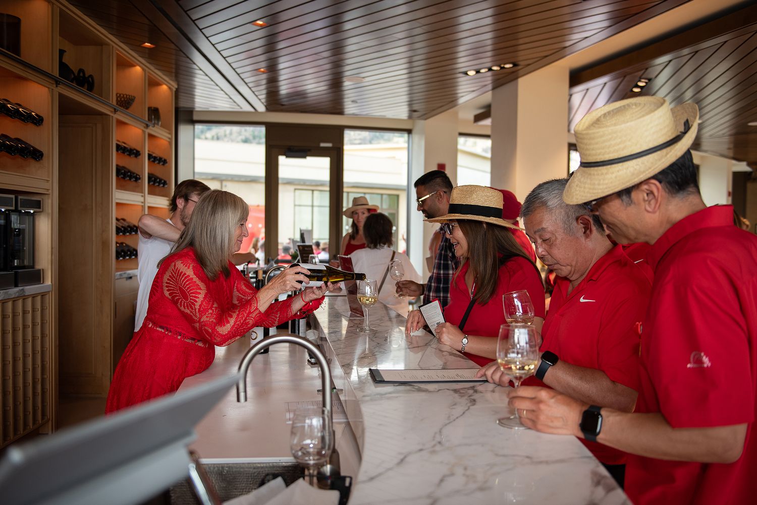 Guests in red shirts enjoy wine tasting at a marble bar counter in an elegant tasting room.