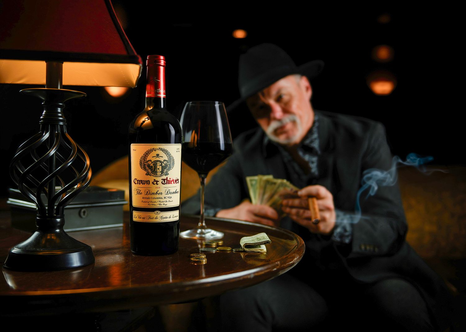 Man in hat counting money beside Creso de Blanco wine bottle and glass on table in dimly lit room.