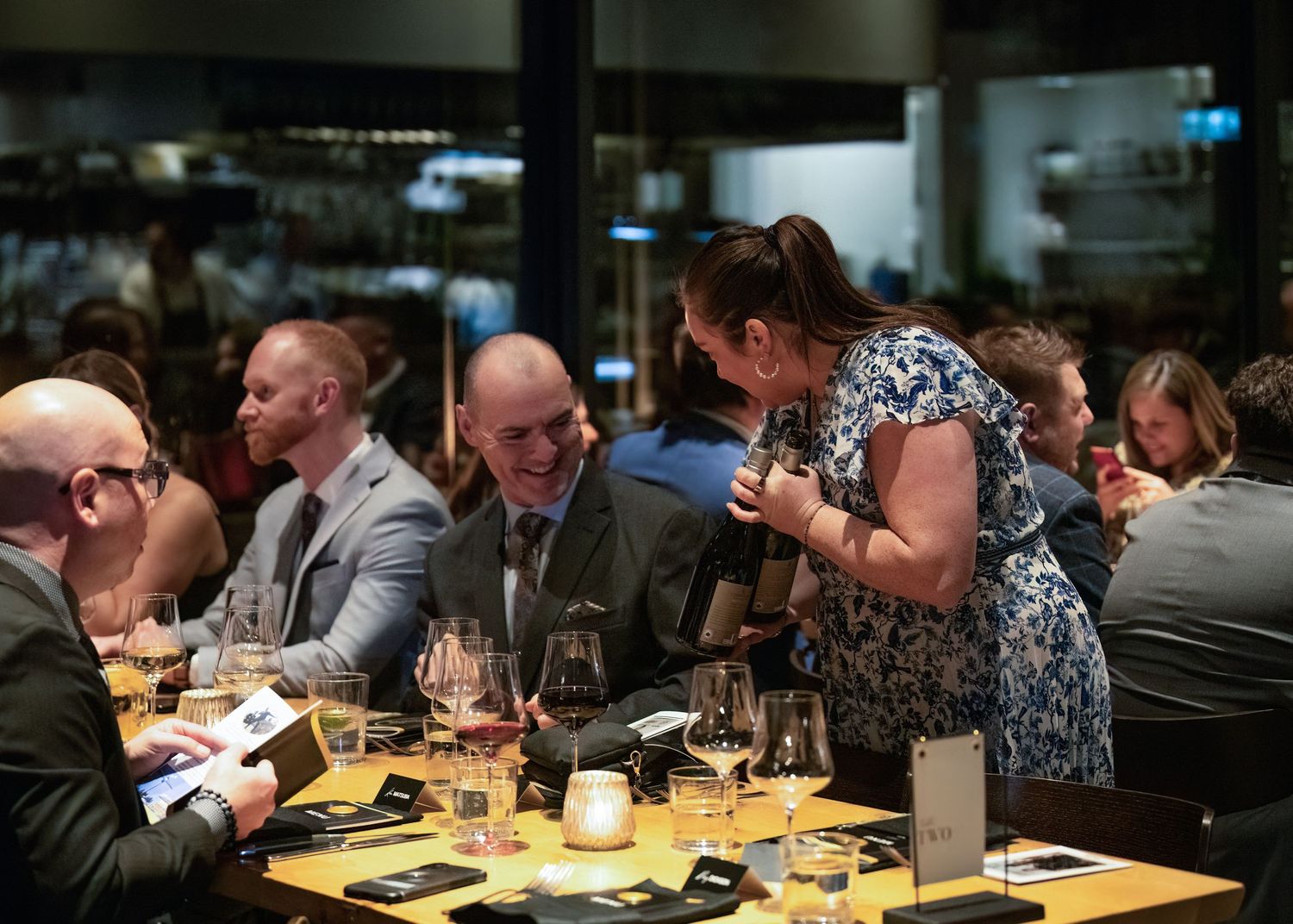 Guests socializing and laughing at a restaurant dinner event with wine glasses on the table.