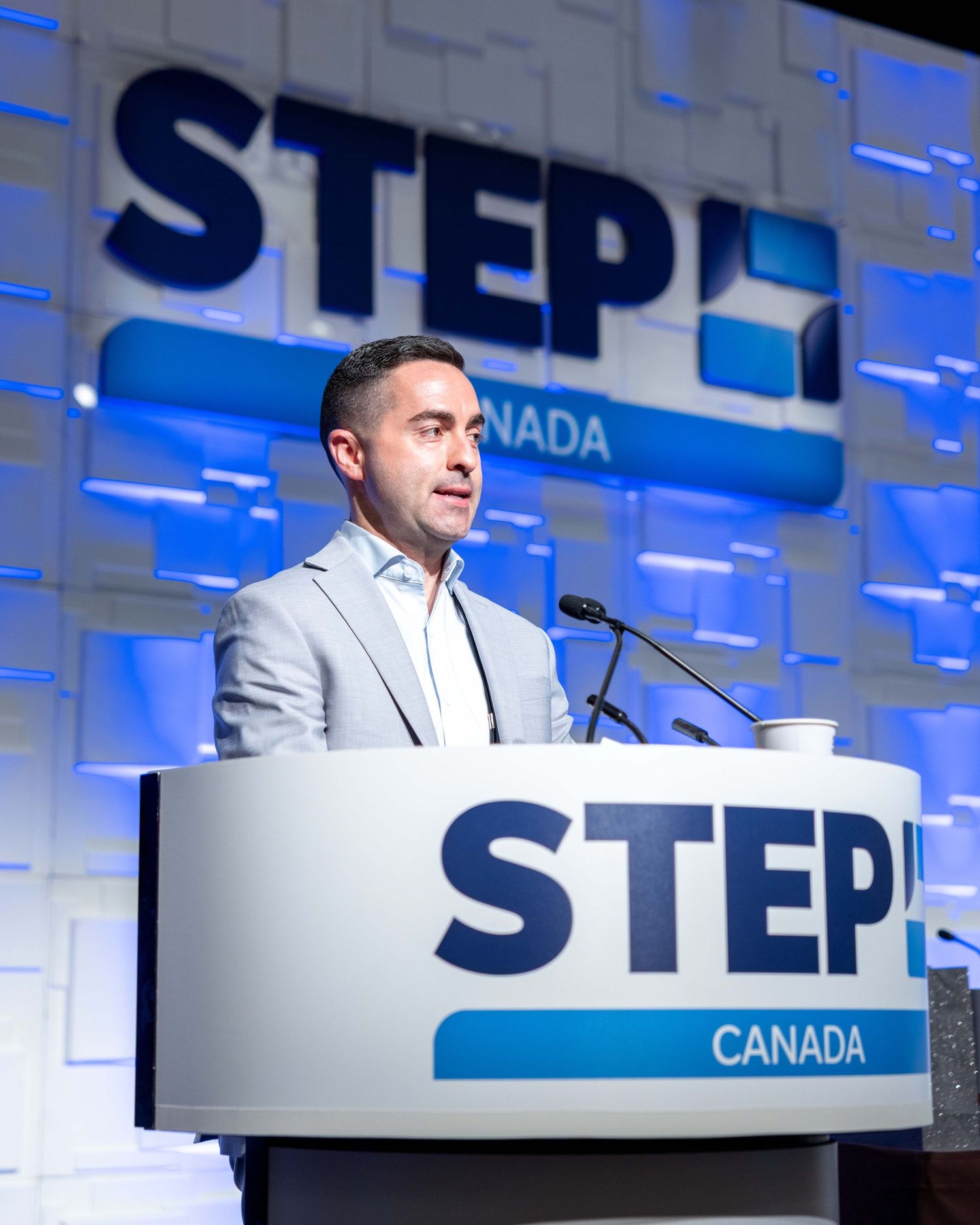 A man in a gray blazer speaks at a STEP Canada podium during a professional conference event.