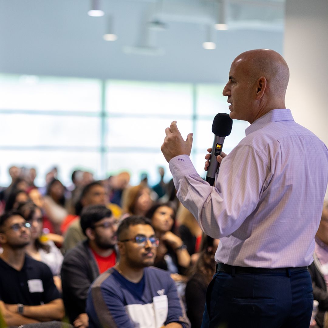 Bald mMpacked corporate event with diverse audience seated in modern venue.