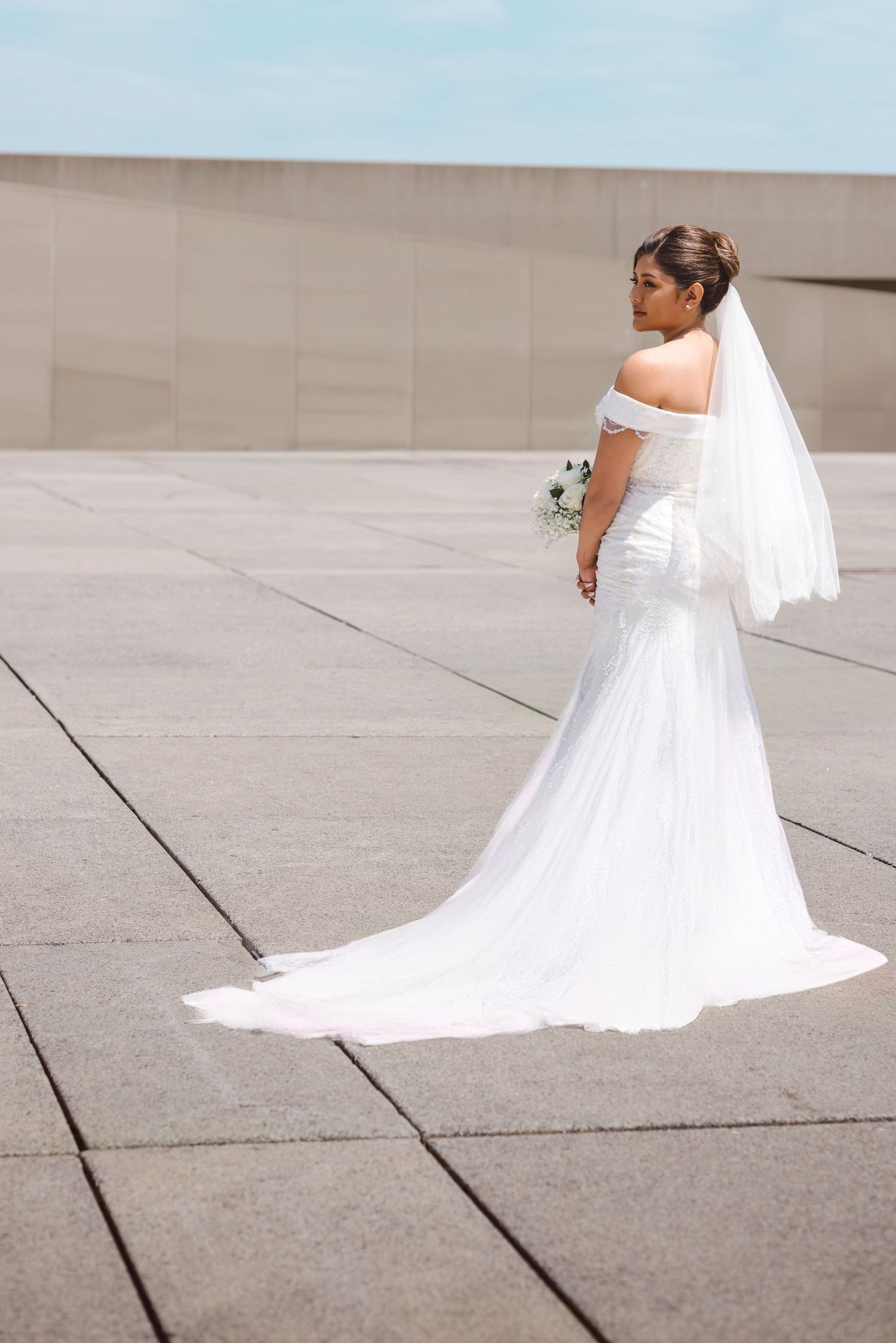 Ethereal bridal portrait showing the dramatic sweep of a white wedding gown's train on concrete pavement.