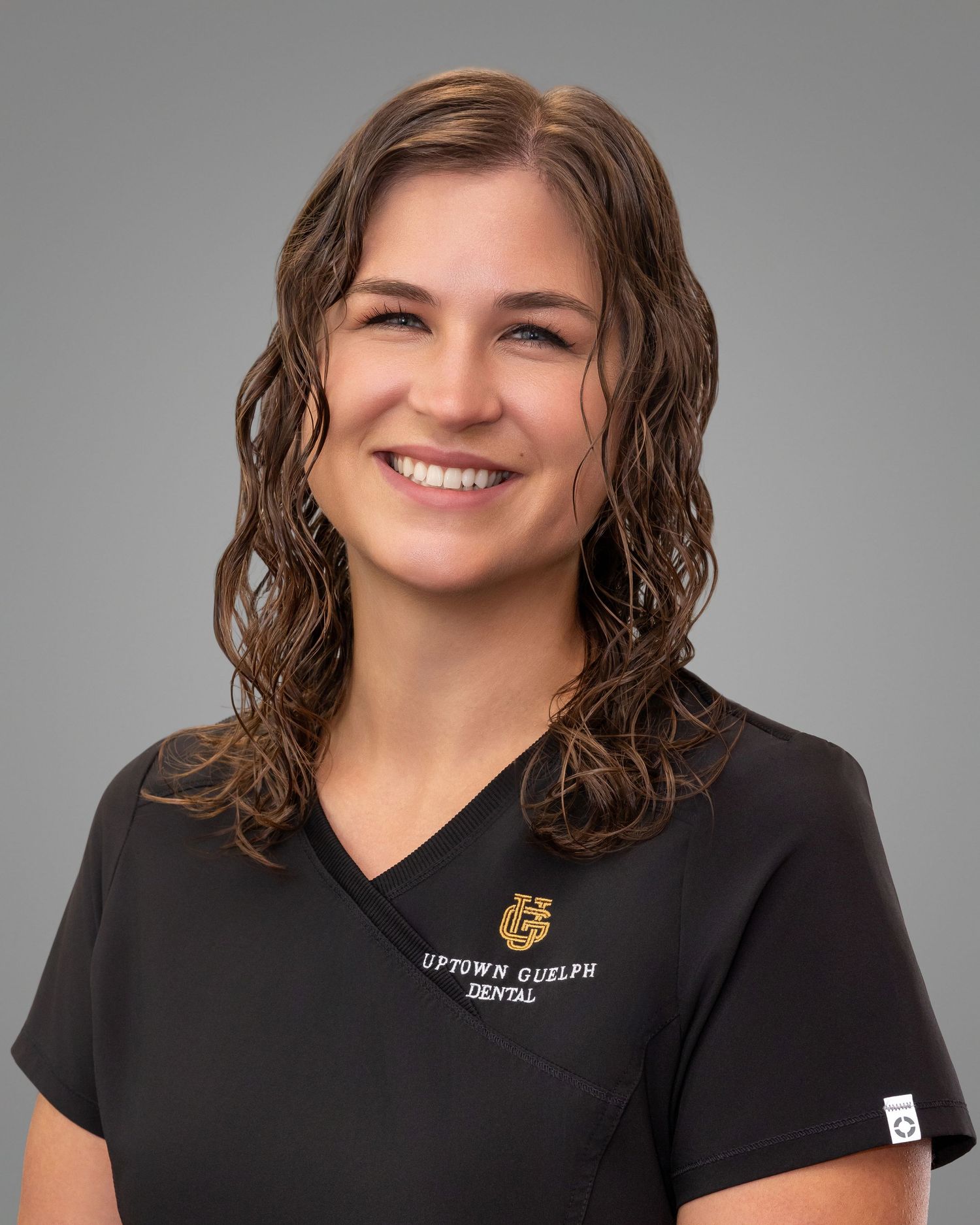 Smiling dental professional in black Uptown Guelph Dental scrubs poses for a headshot photo.