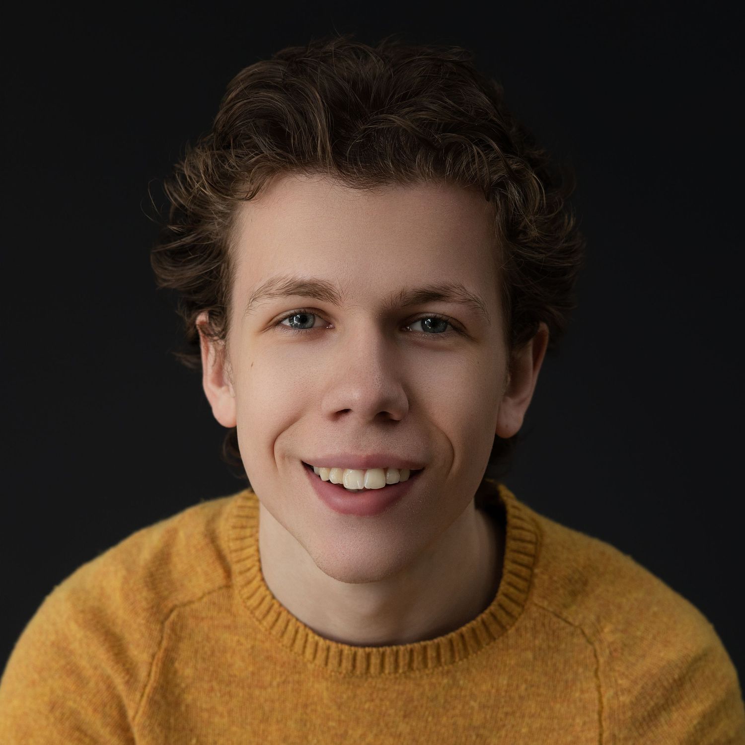 Young person wearing a yellow sweater smiling in a series of closeup portraits against dark background.