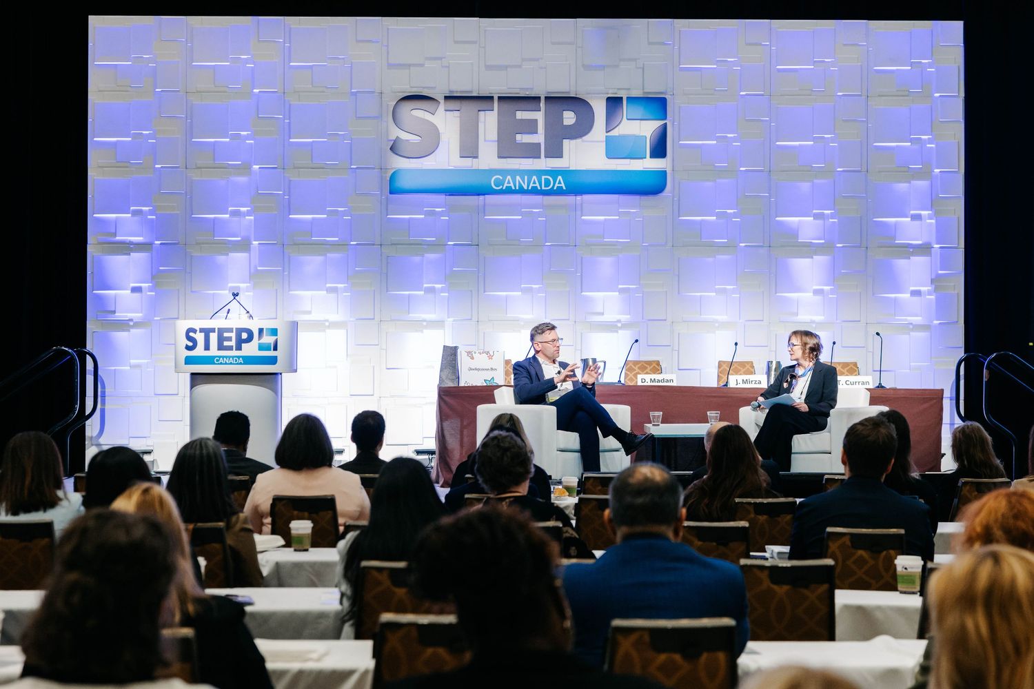 Two speakers in discussion on stage at STEP Canada conference with seated audience in foreground.