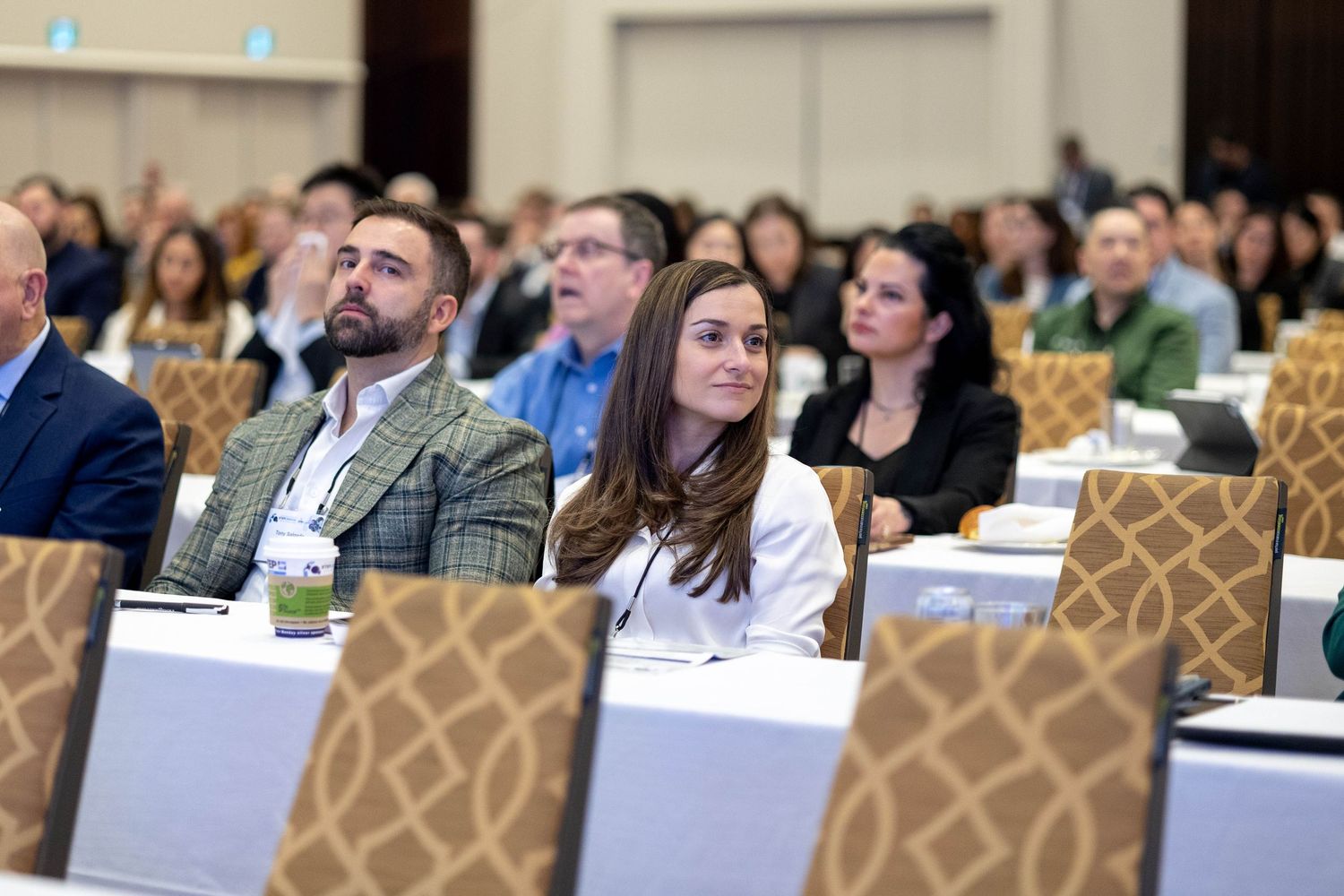 Professionals attentively listening at a corporate conference in a modern hotel ballroom with rows of tables.
