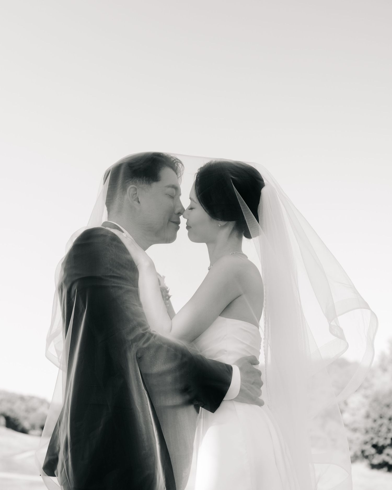 Black and white wedding photo of bride and groom sharing an intimate moment under a veil outdoors.