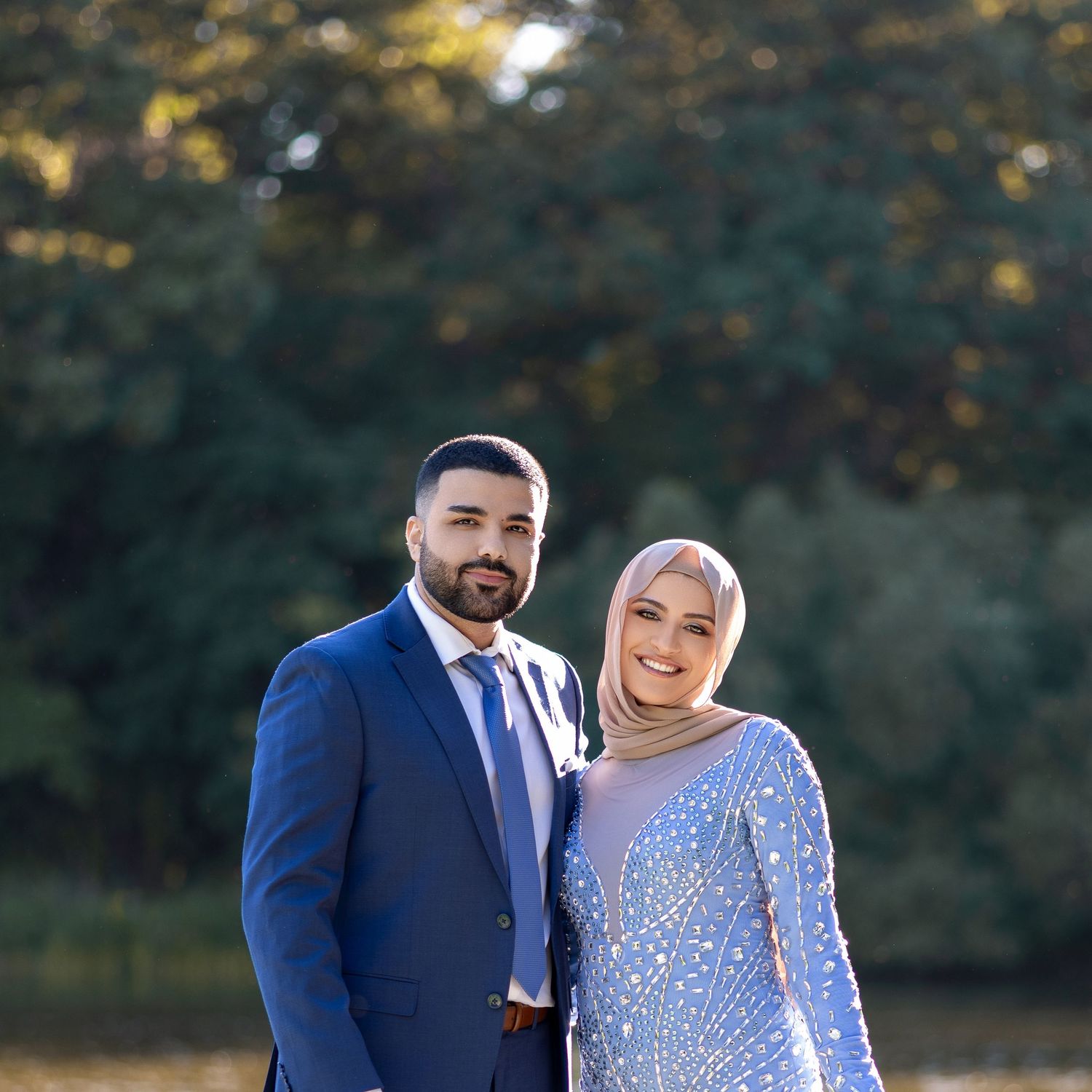 A couple poses outdoors in formal attire with navy suit and silver sequined dress during sunset photoshoot.