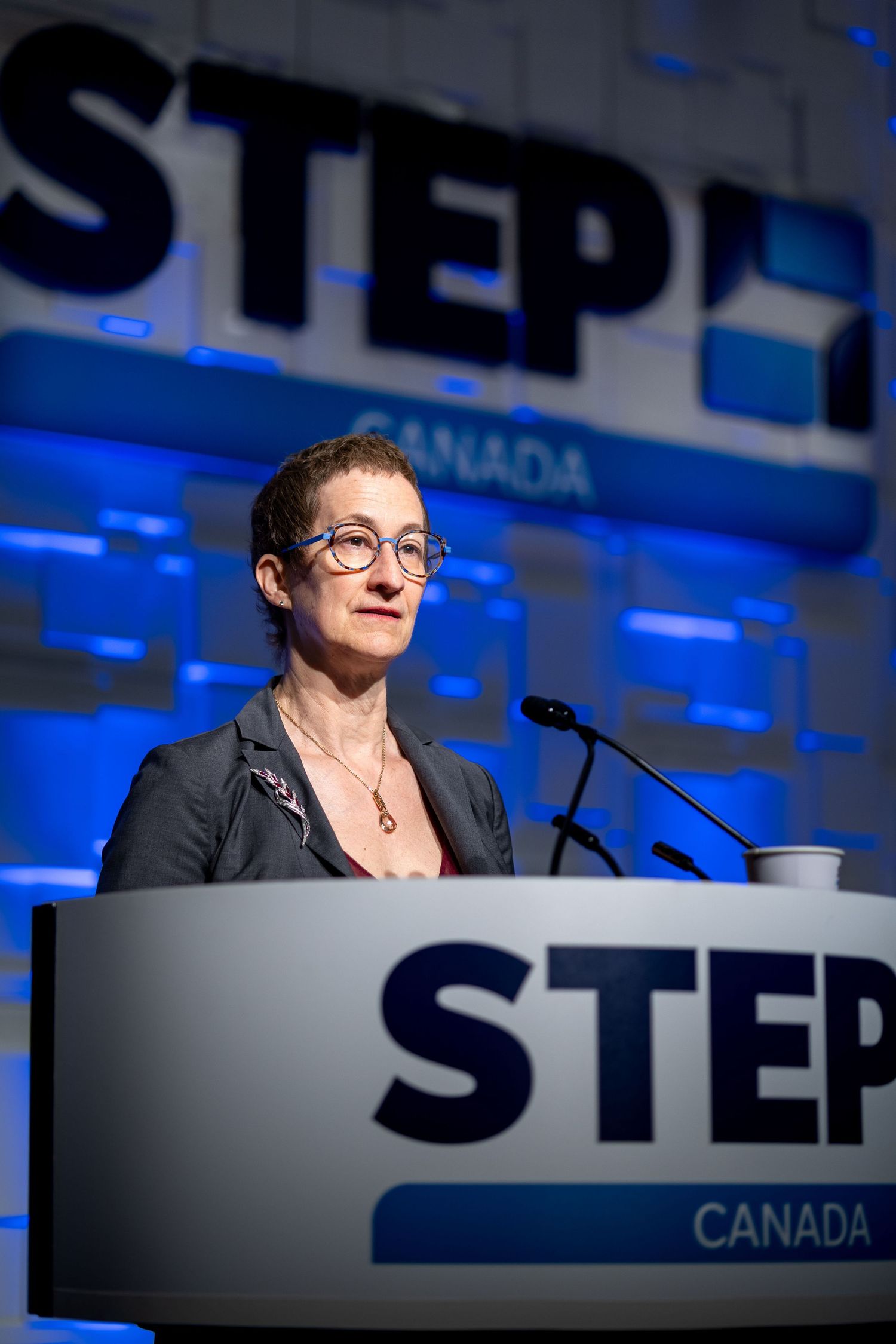 Woman speaking at STEP Canada conference podium on stage with blue illuminated backdrop.