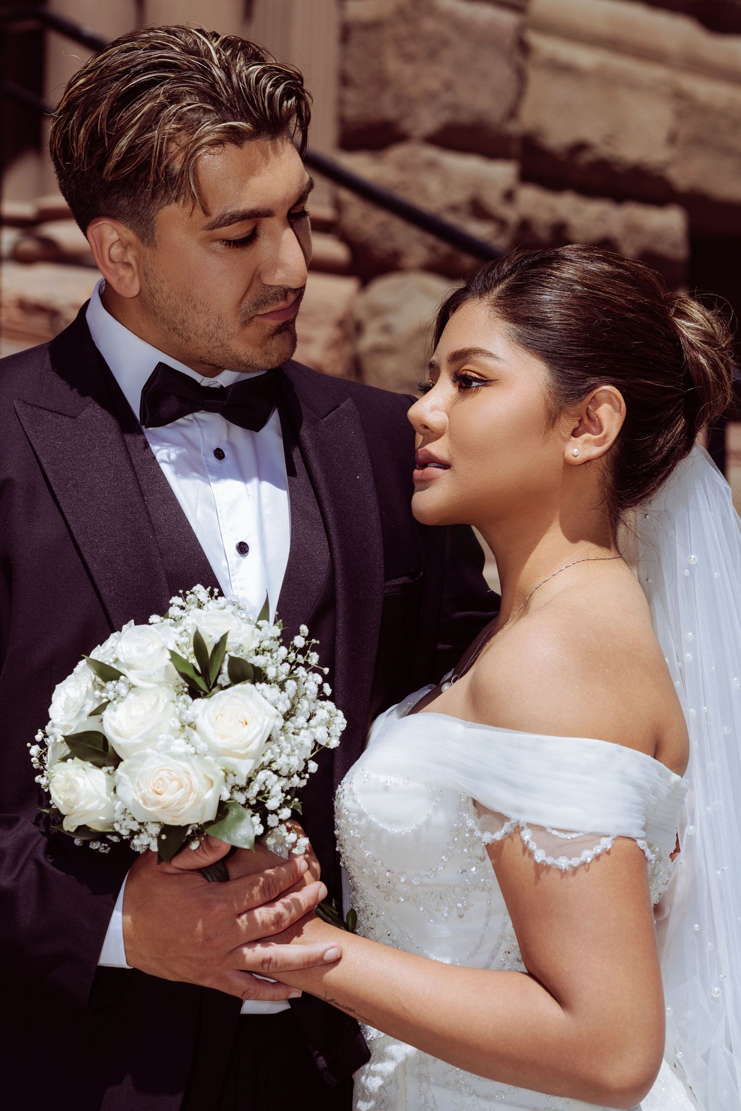 Romantic wedding photos showing intimate moments between newlyweds holding white roses and baby's breath bouquet.