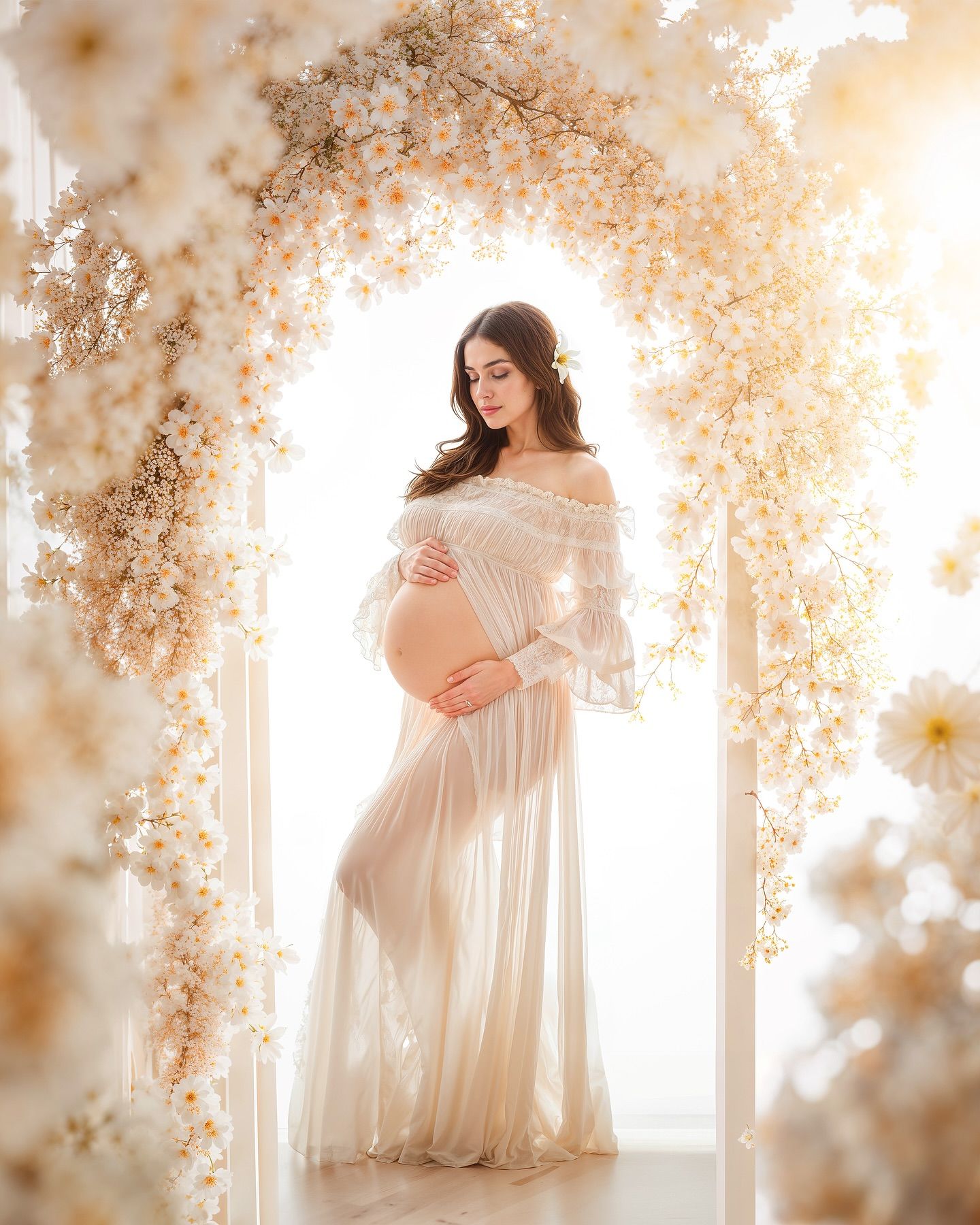 Ethereal maternity photo with soft white dress and floral arch creating dreamy atmosphere in natural light.