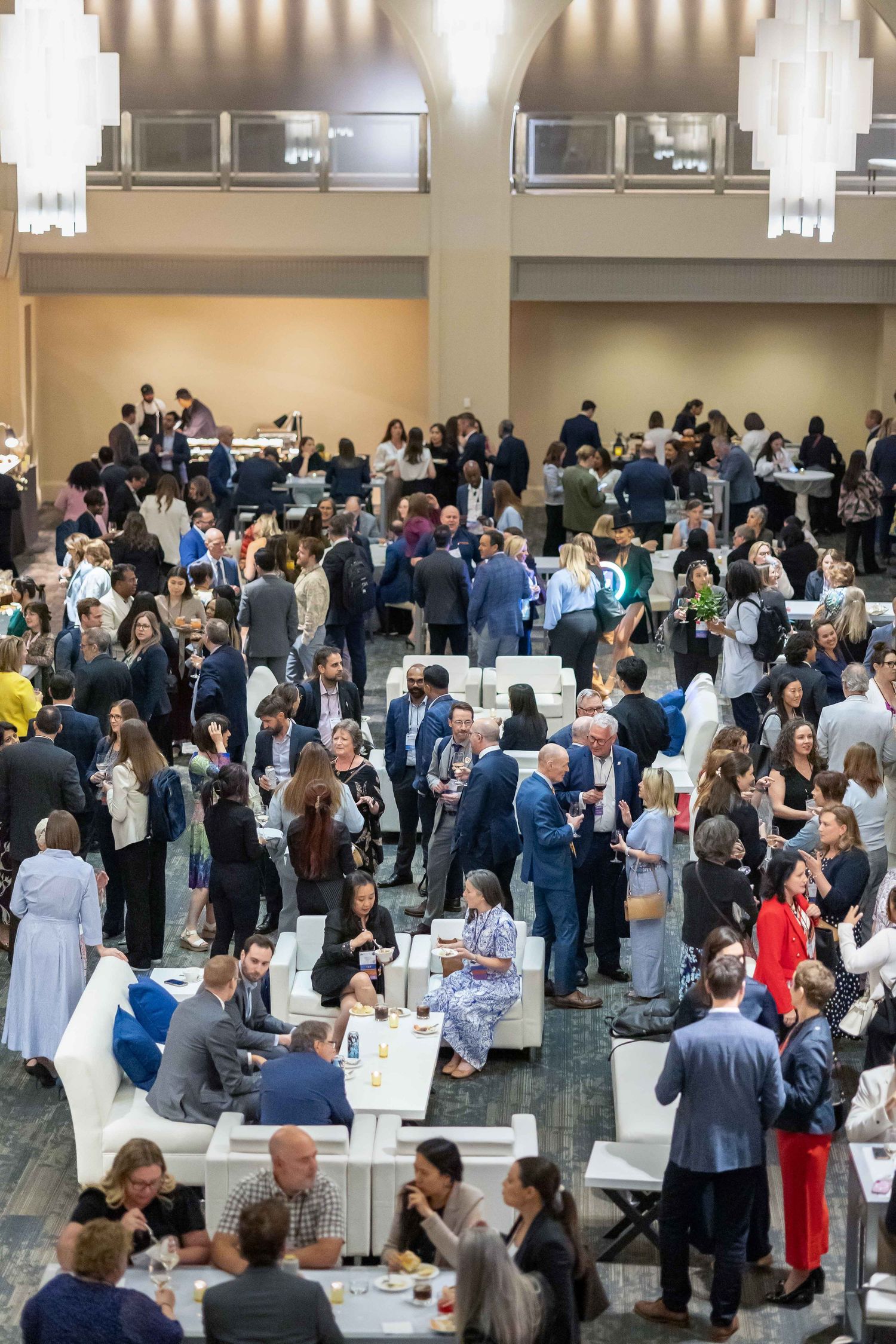 Large professional networking event with hundreds of attendees mingling in a modern conference hall with white furniture.