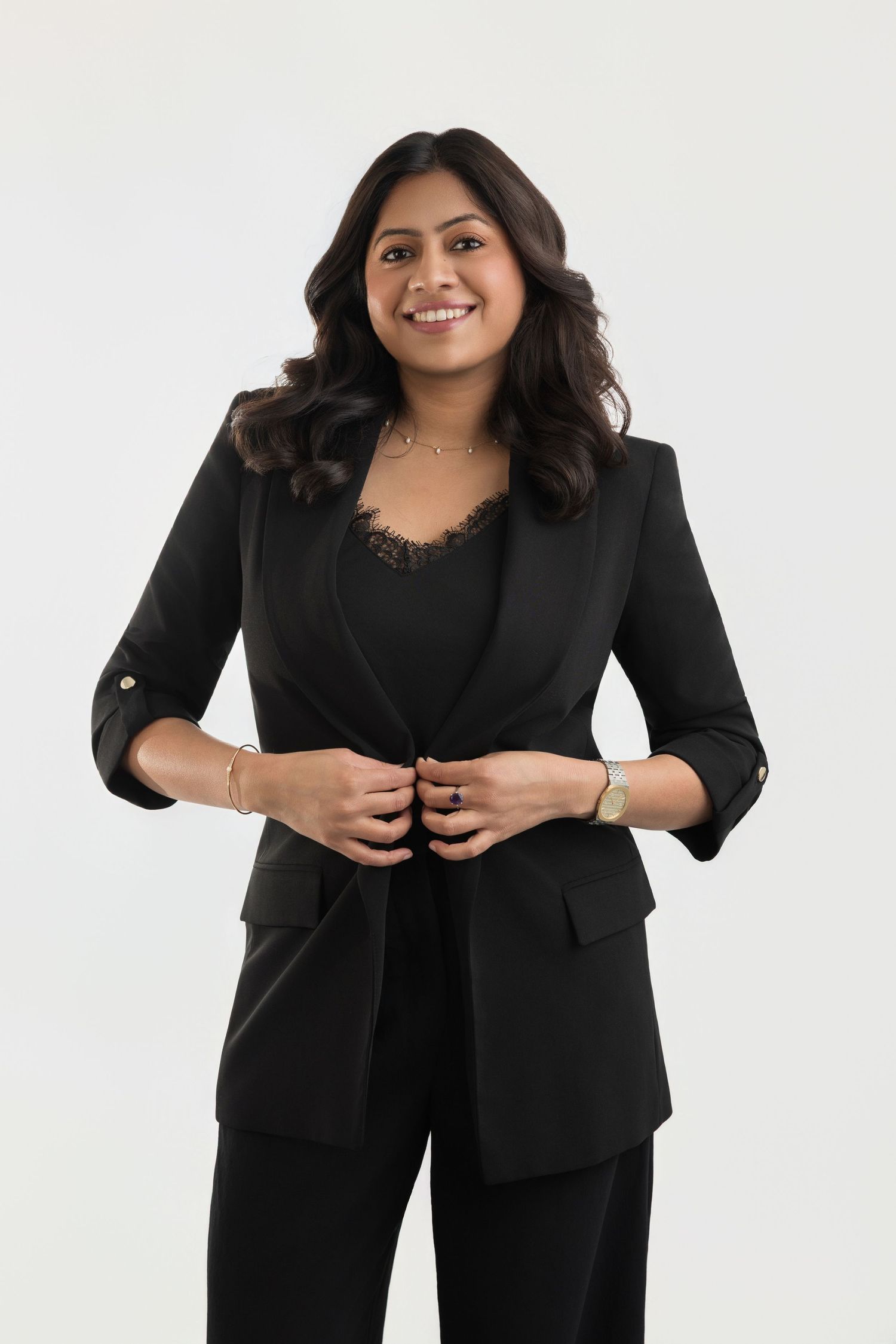 Woman in black blazer and pants smiling confidently against white background.