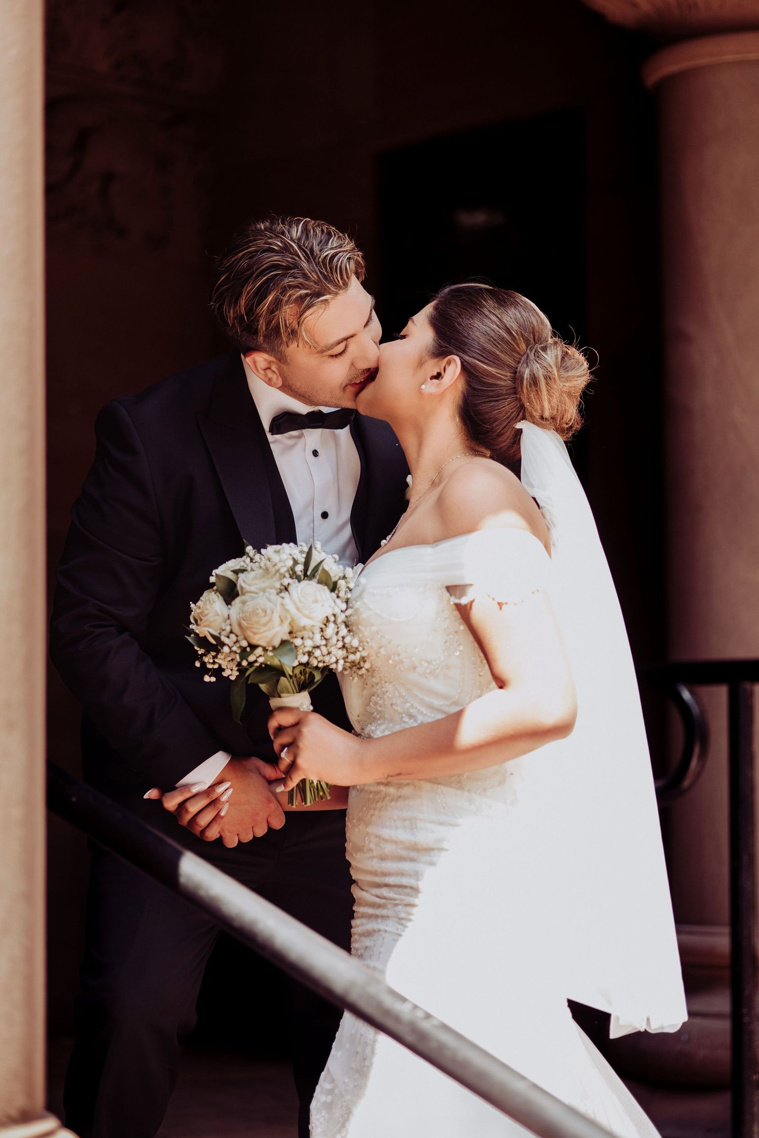 Newlywed couple share romantic kiss at wedding ceremony while bride holds elegant white floral bouquet.