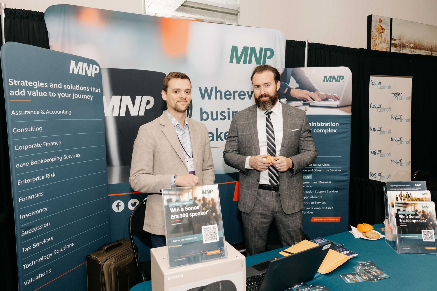 Two professionals stand at an MNP consulting firm trade show booth displaying business services and branding materials.