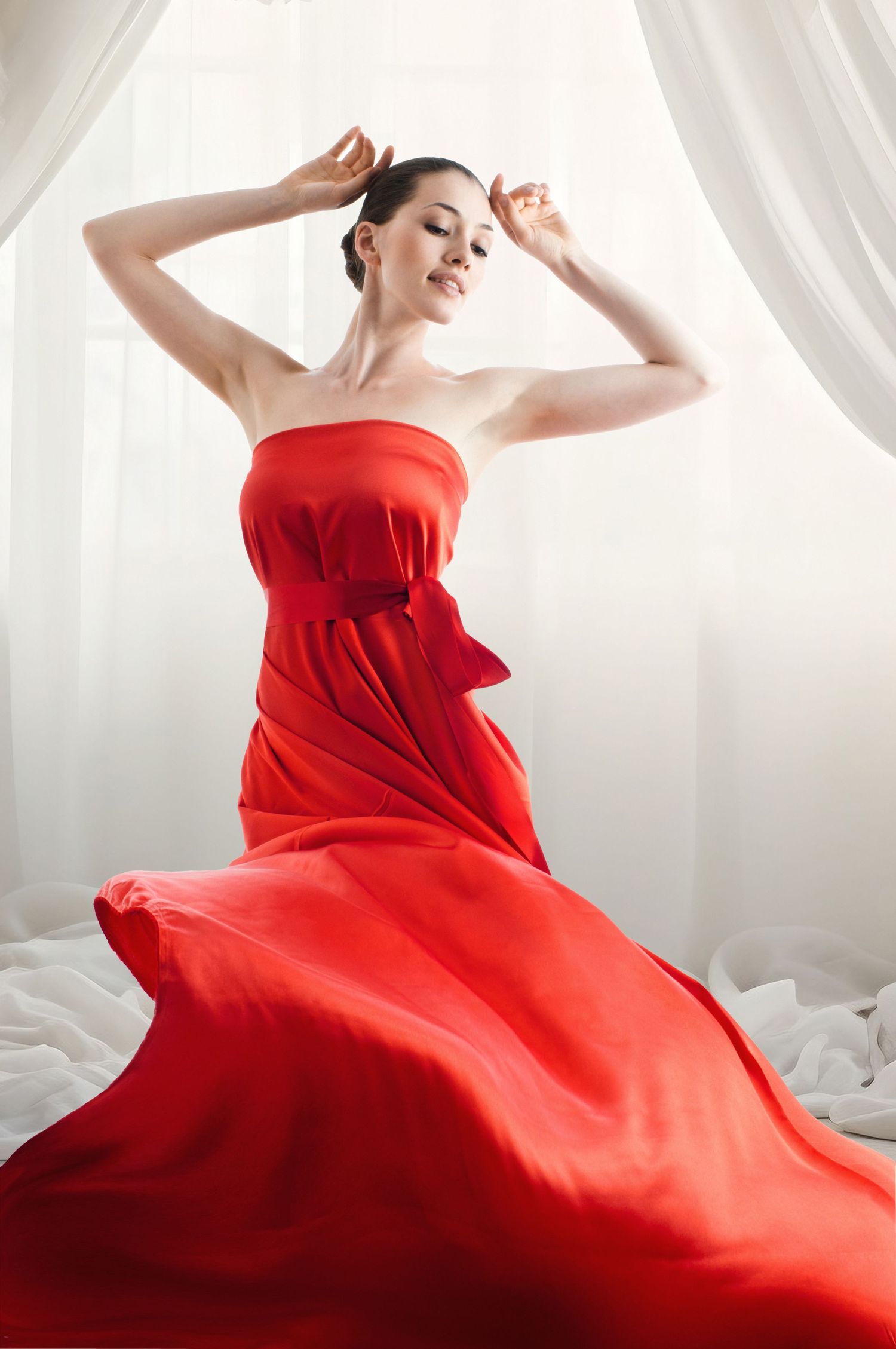 A graceful figure in a flowing red dress poses elegantly against white curtains in a dynamic photo series.