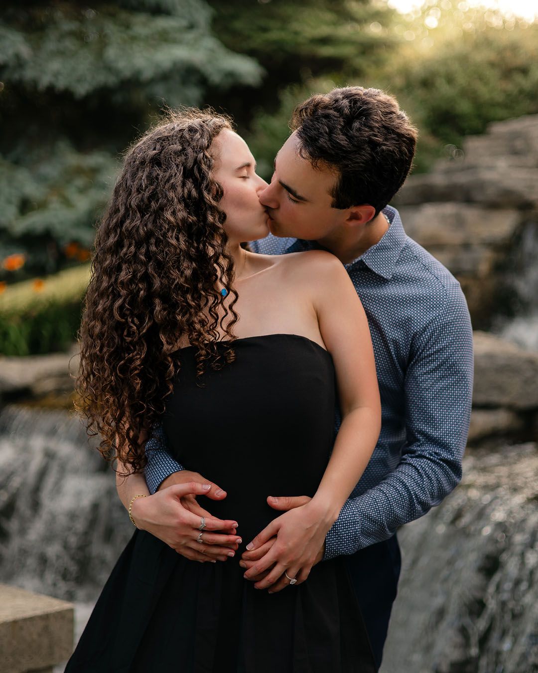 A couple shares a tender embrace against a scenic sunset backdrop at a rocky overlook.