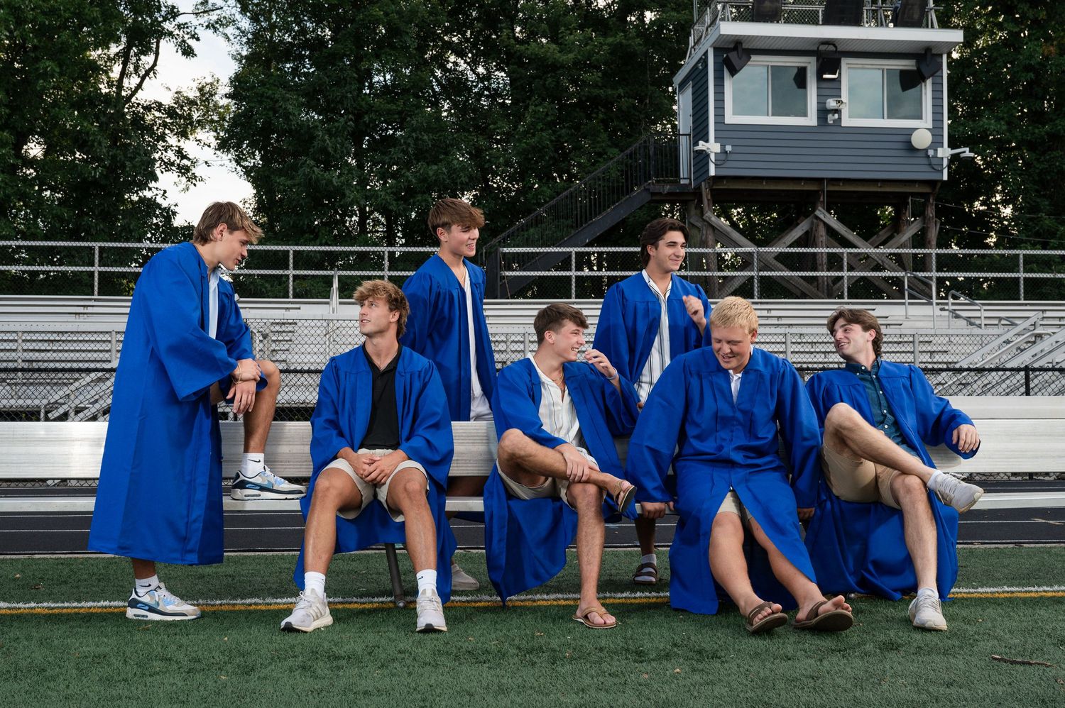 Students in royal blue graduation robes gathered on stadium bleachers for a casual group photo.