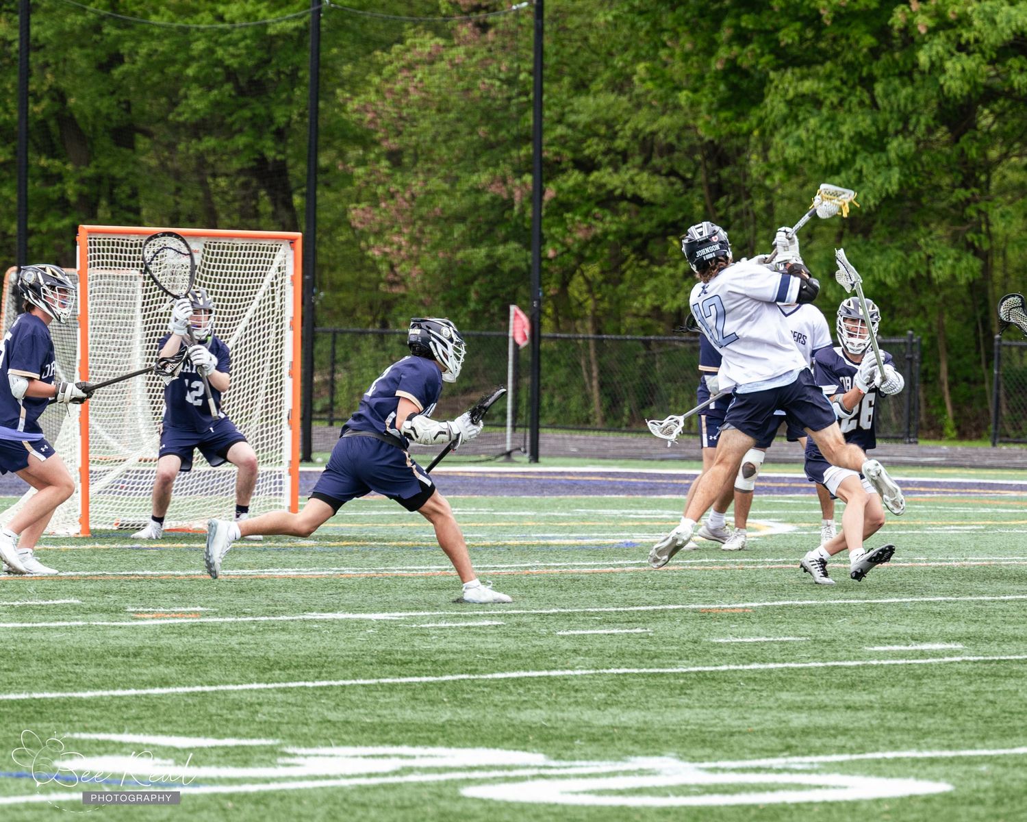 Lacrosse players practicing drills on artificial turf field with goal nets visible.