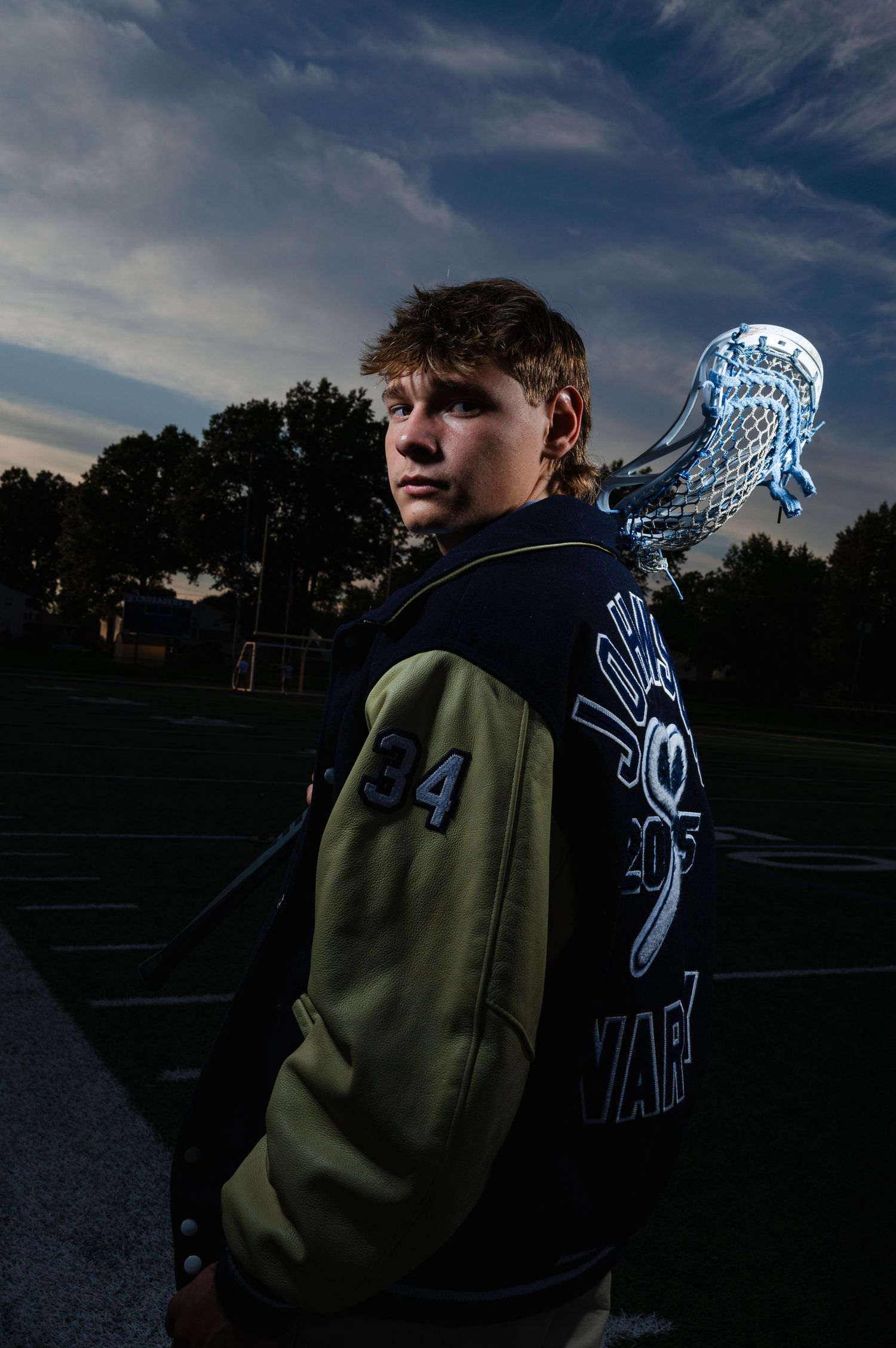 Athletic portrait of player in varsity jacket at dusk on sports field.