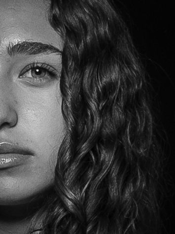 Close-up black and white portrait of someone with wavy hair and dramatic lighting.