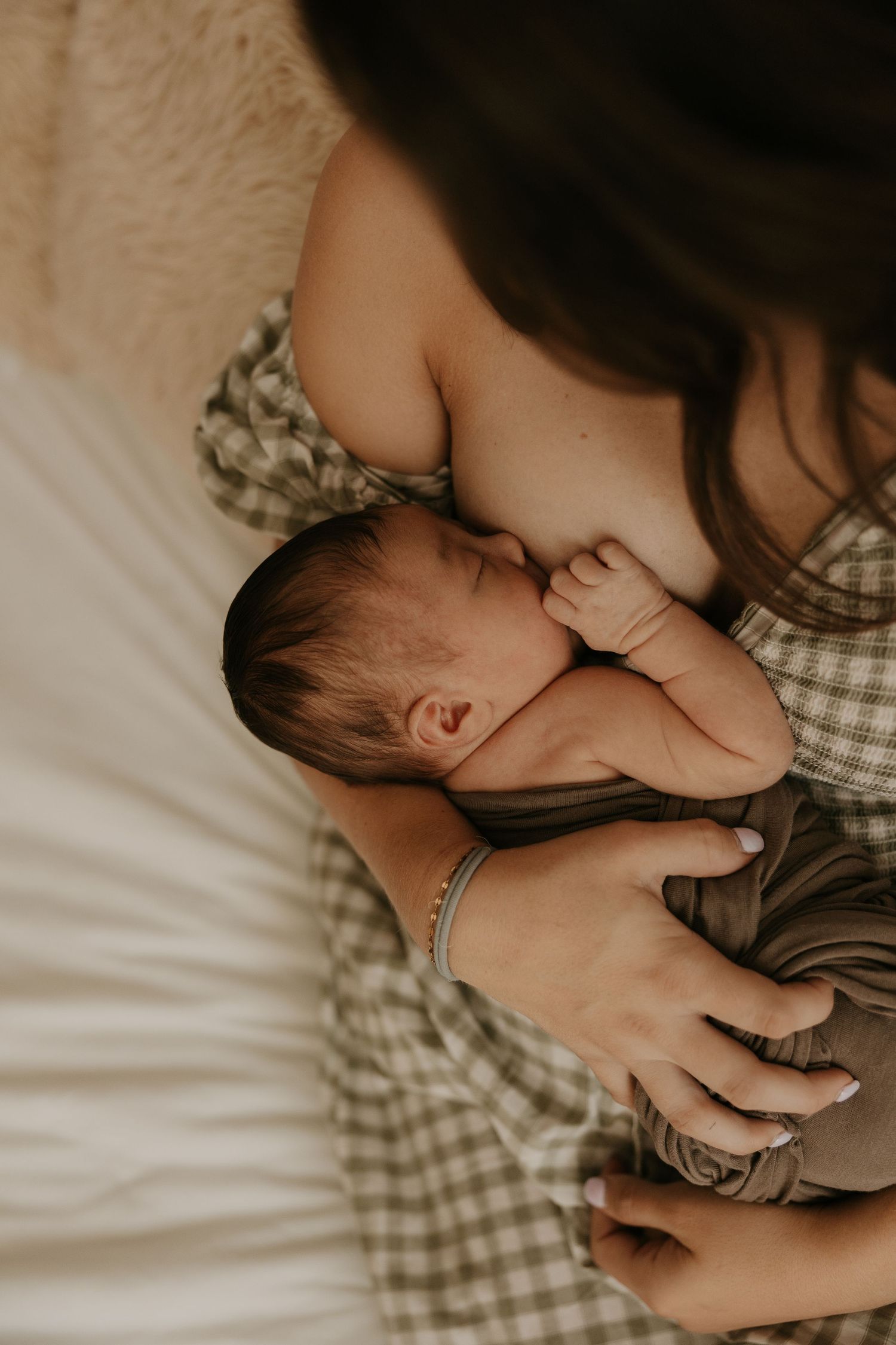 A mother breastfeeding her newborn baby while cradling the infant in her arms on a white bed.