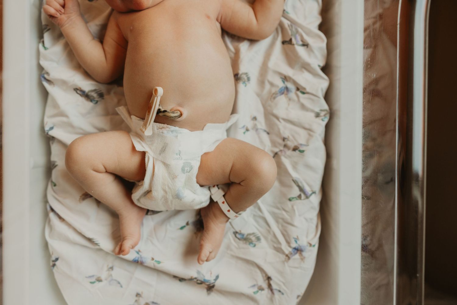Newborn baby lying on back in a crib wearing a cloth diaper on a floral patterned blanket.