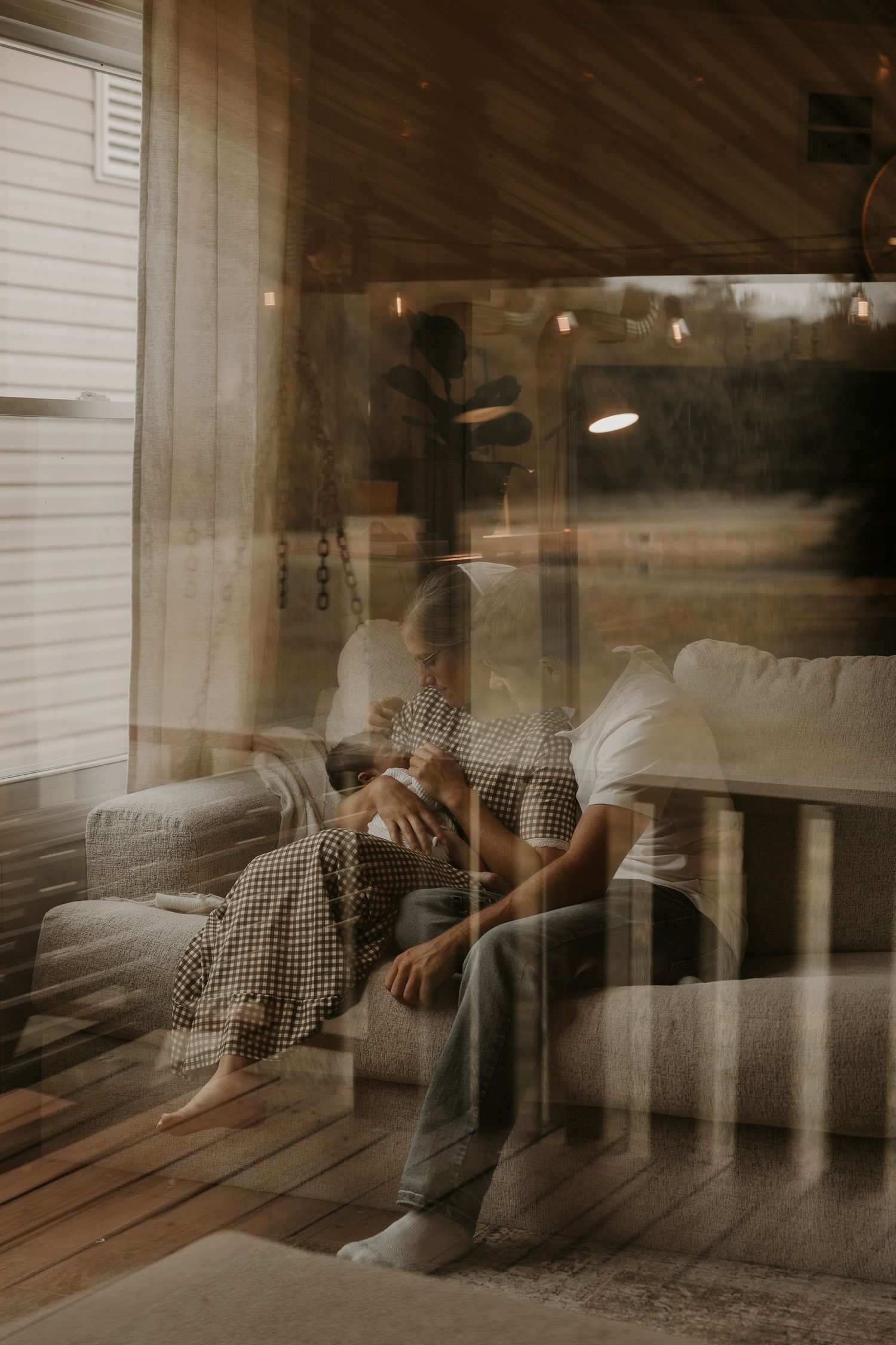 Couple sitting together on a couch, captured through glass with a dreamy double exposure effect in a cozy cabin.