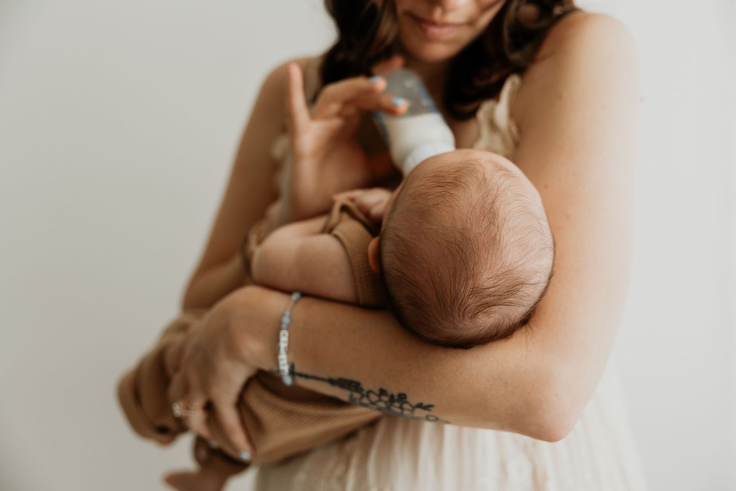 A mother tenderly cradles her newborn baby in her arms, wearing bracelets, against a soft white background.