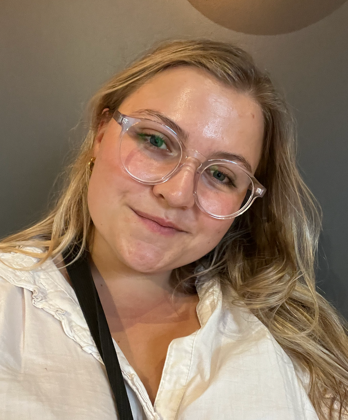 Smiling woman with blonde wavy hair wearing clear-frame glasses and white shirt selfie portrait.