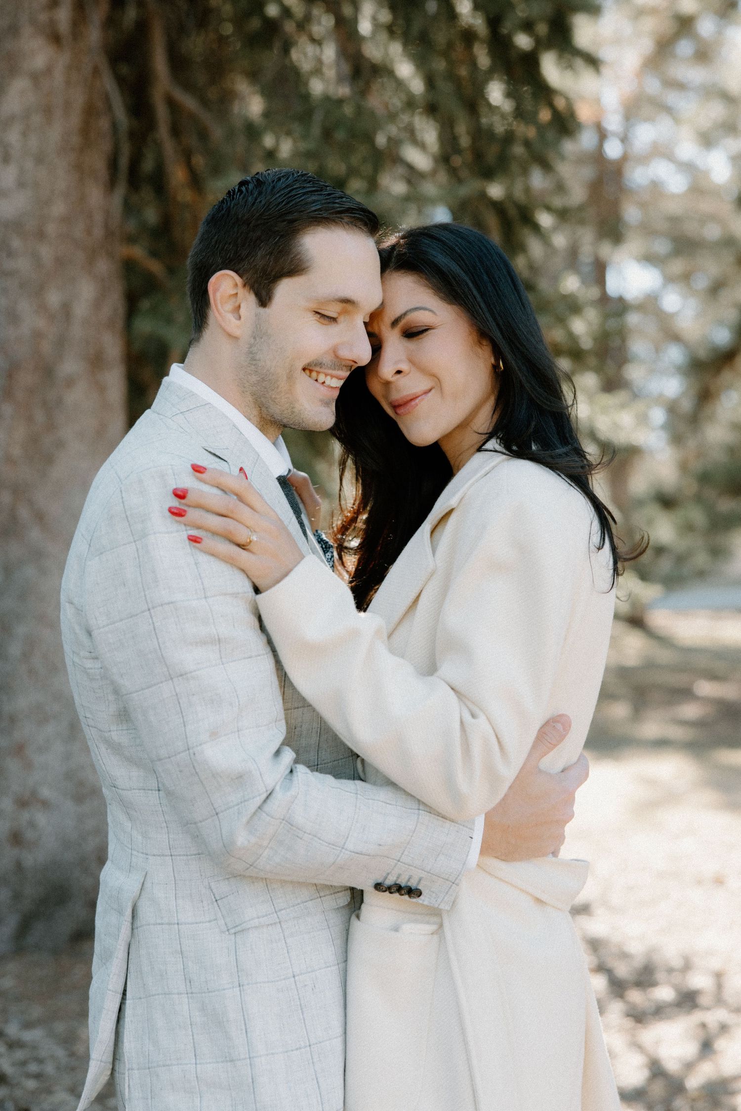 Romantic winter engagement photos of couple in matching white outfits among trees.