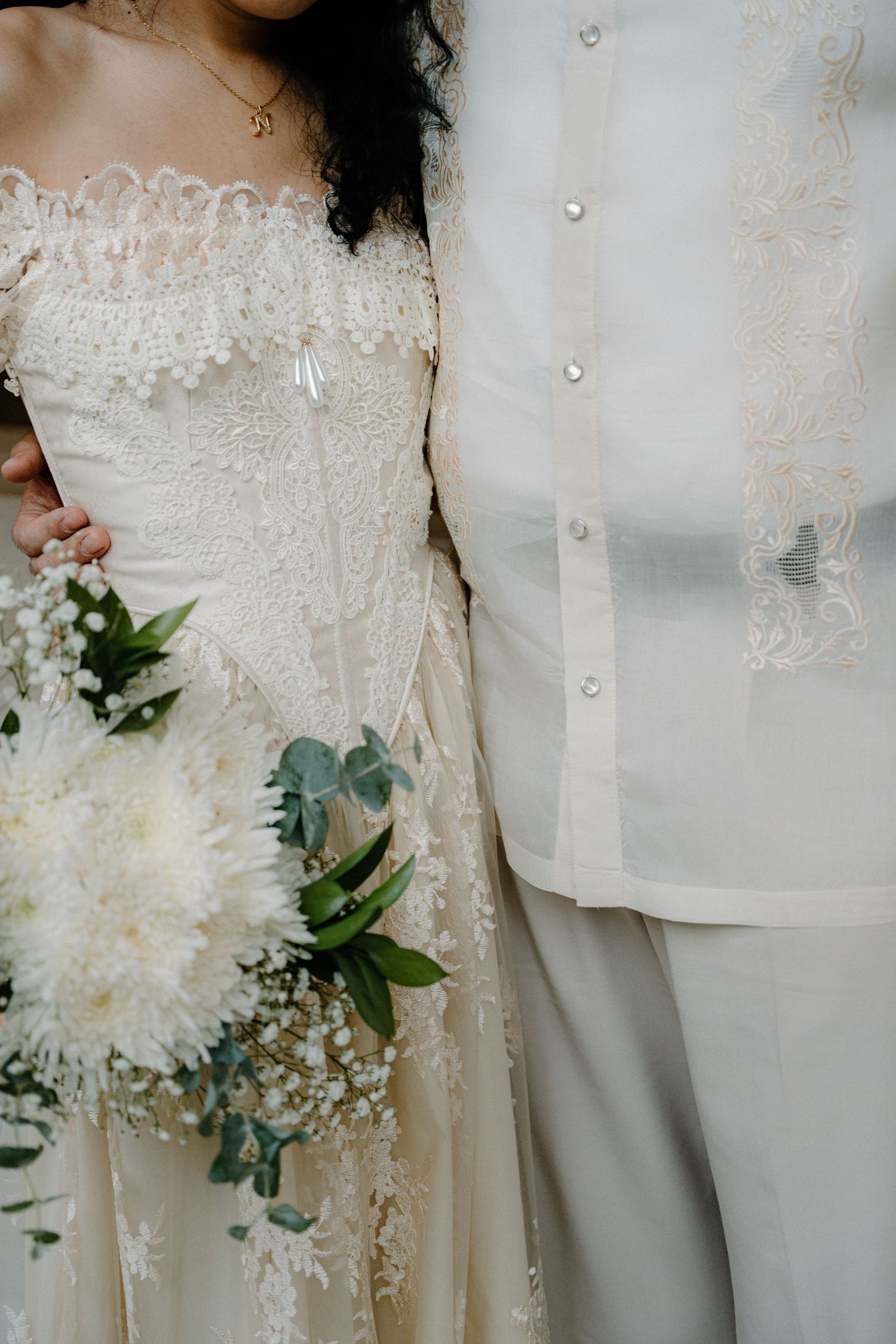 Close-up details of delicate white lace wedding dress with buttons and floral bouquet featuring eucalyptus leaves.