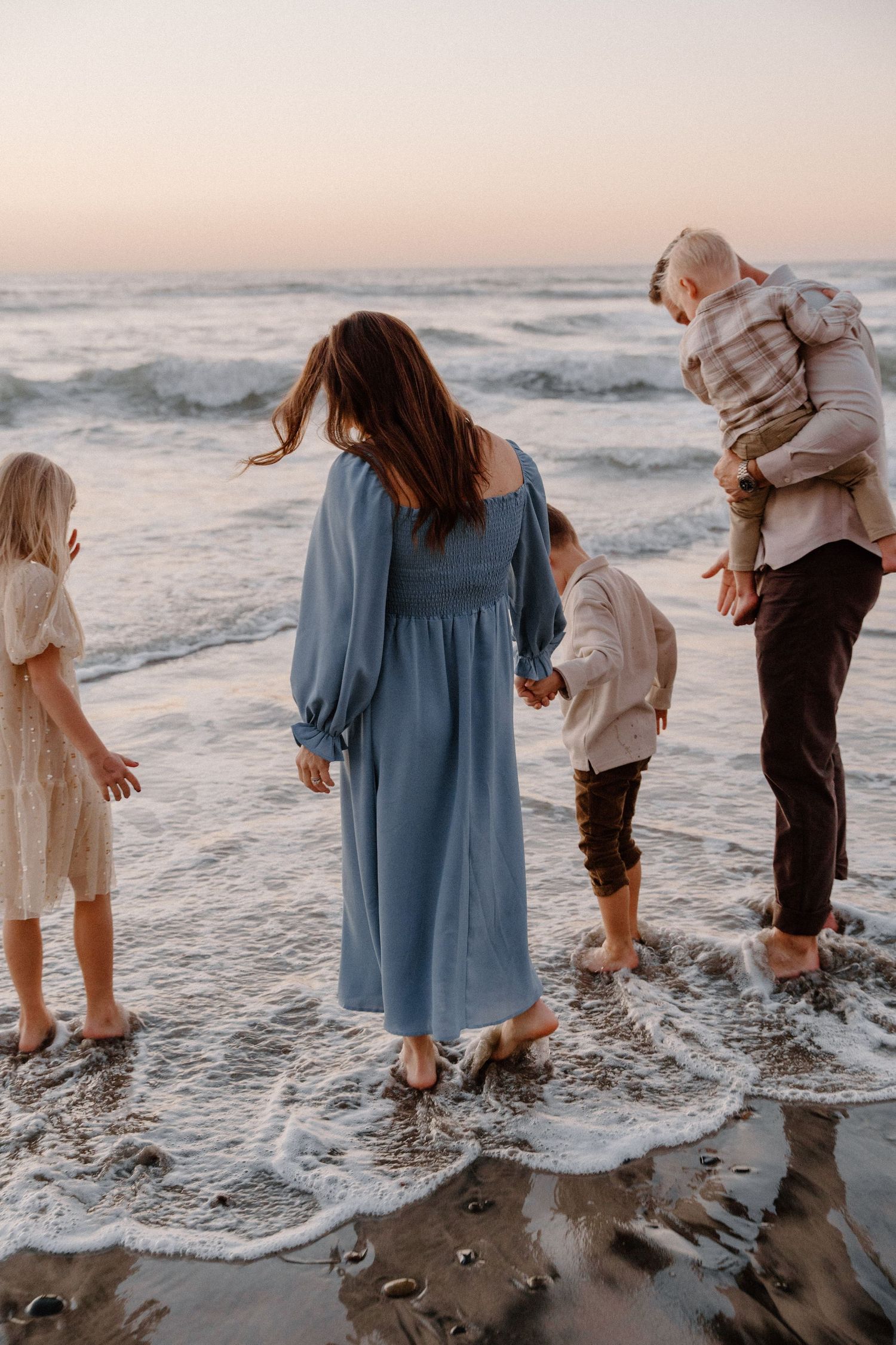 Family enjoying waves together on beach at sunset in casual attire  at Torrey Pines in San Diego, CA.