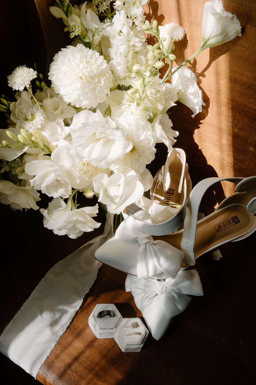 White carnations in an elegant vase with a white ribbon bow cast soft shadows on a wooden surface in natural light.