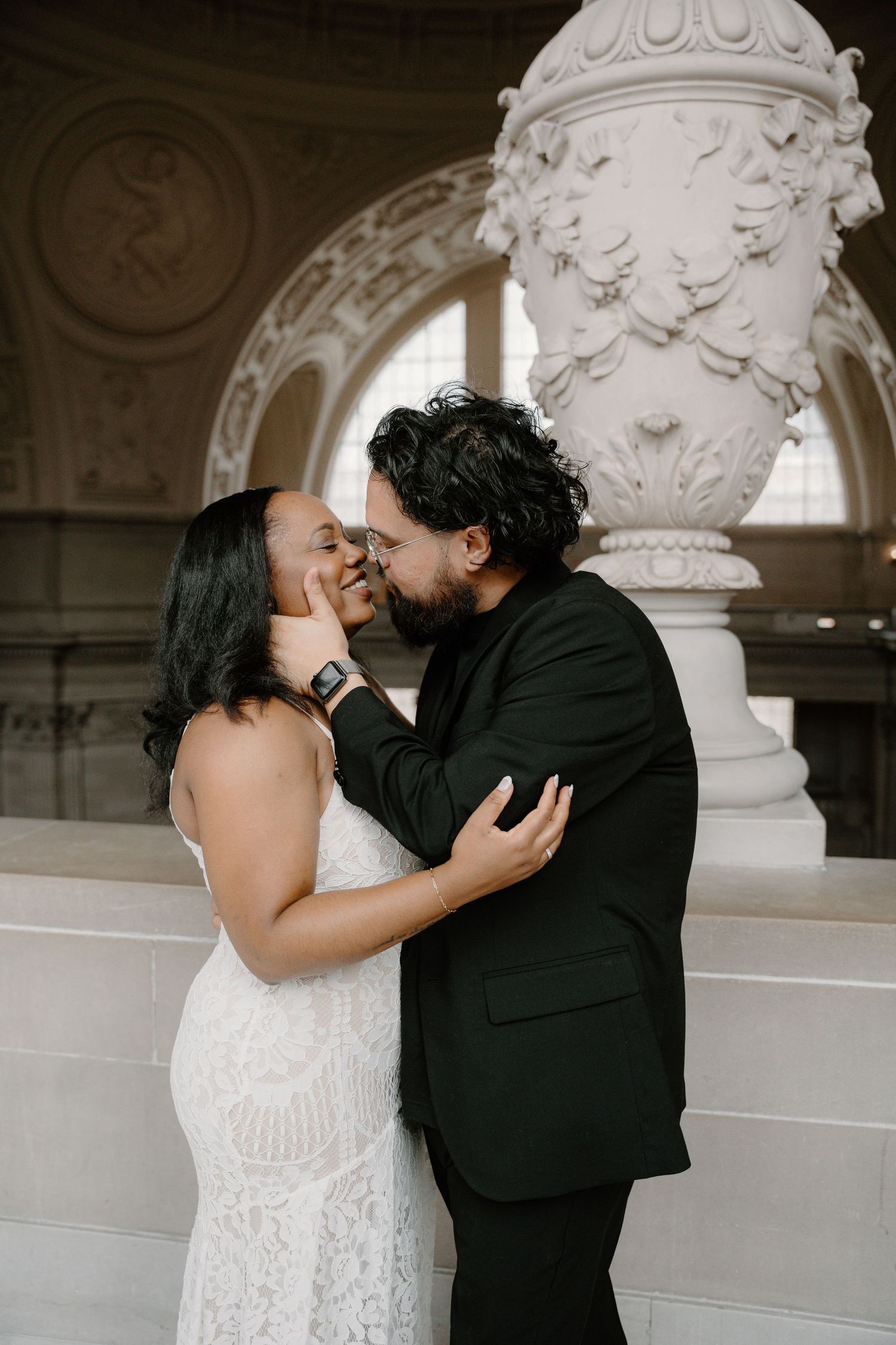 A tender moment between a couple in formal wear beside an ornate marble pillar at San Francisco City Hall.