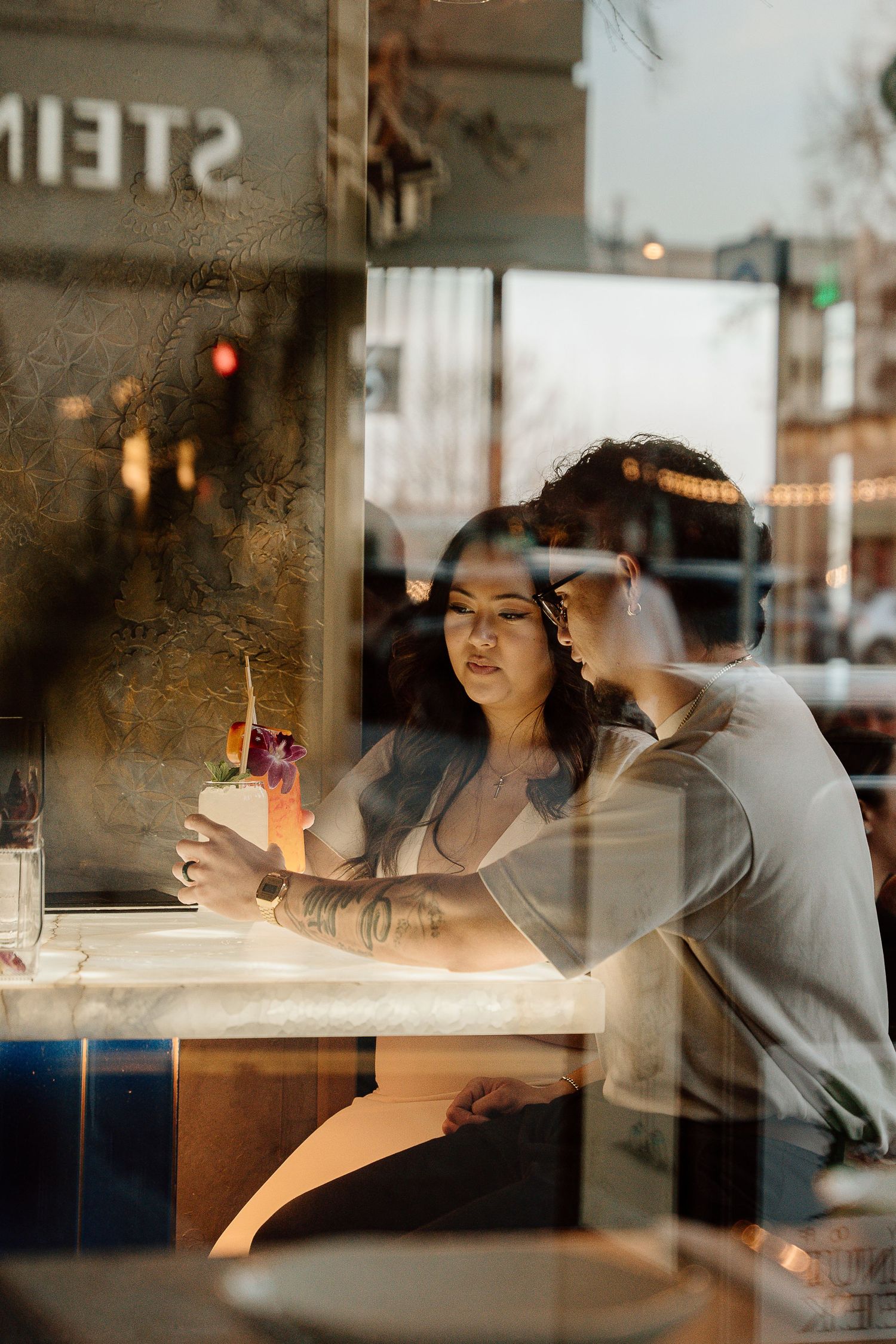 Two people share drinks at a marble bar top seen through a window reflection in downtown Brentwood, CA.