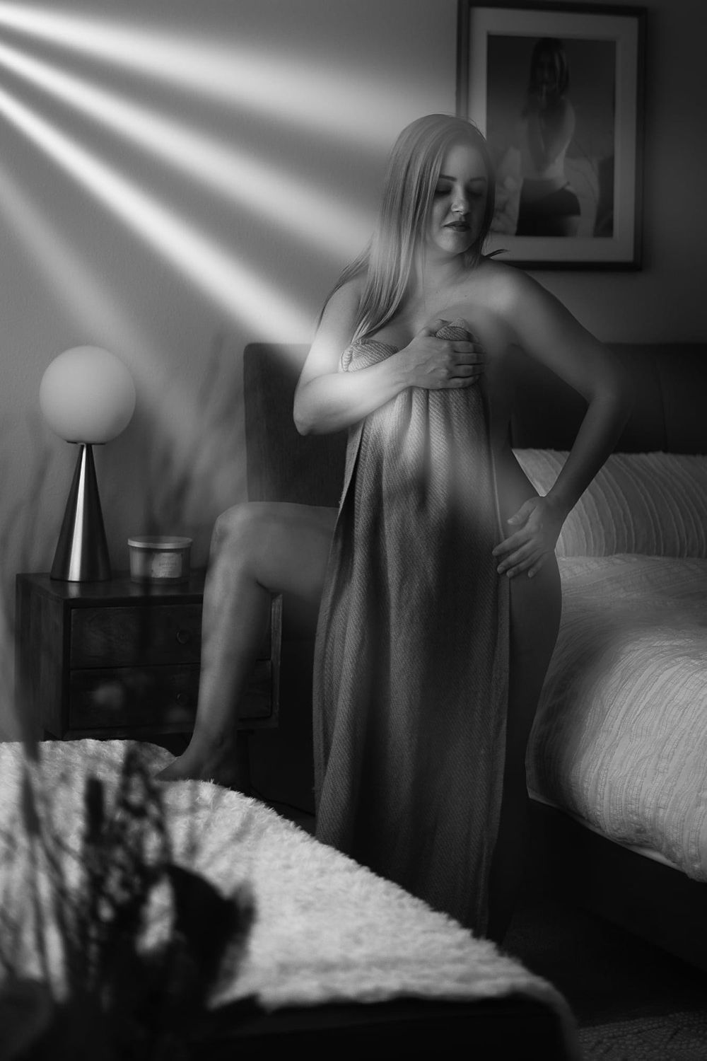 Artistic boudoir photo with dramatic light beams streaming through window in monochrome.