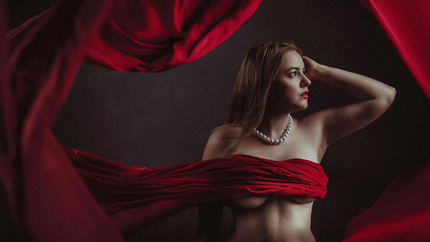 Artistic boudoir photography with flowing red fabric creating dramatic effect.