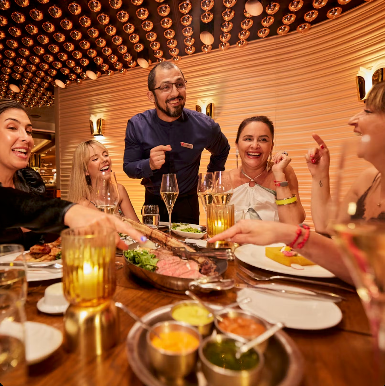 A group enjoying dinner and drinks at a restaurant with warm lighting and festive atmosphere.