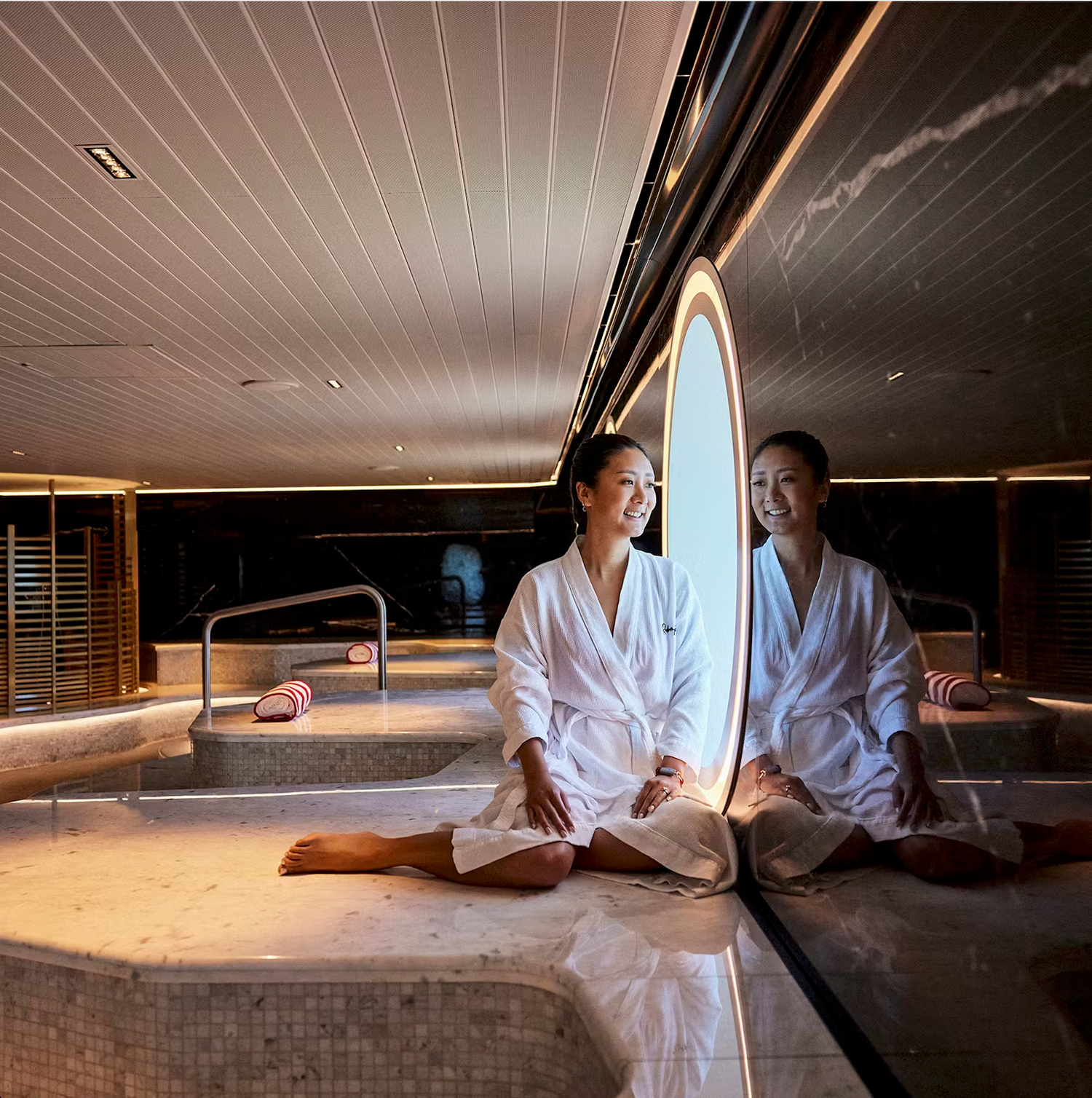 Two people in white robes relax in a dimly lit spa setting with surfboards and tranquil ambiance.