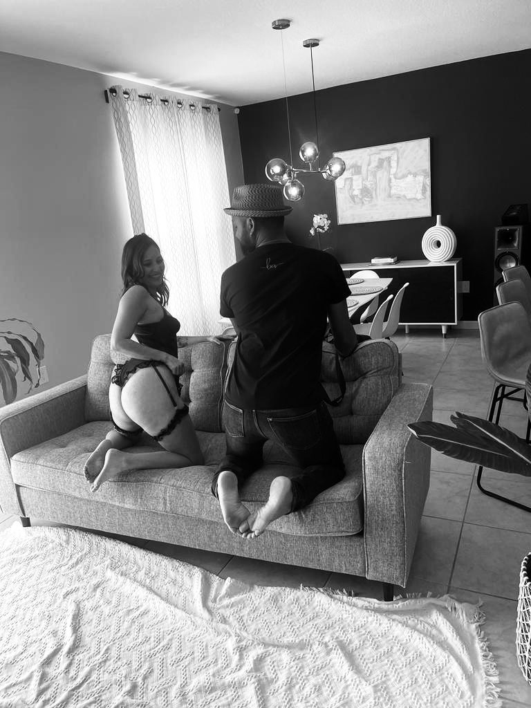 Black and white photo of people kneeling on a couch in a modern living room with pendant lights and artwork on the wall.