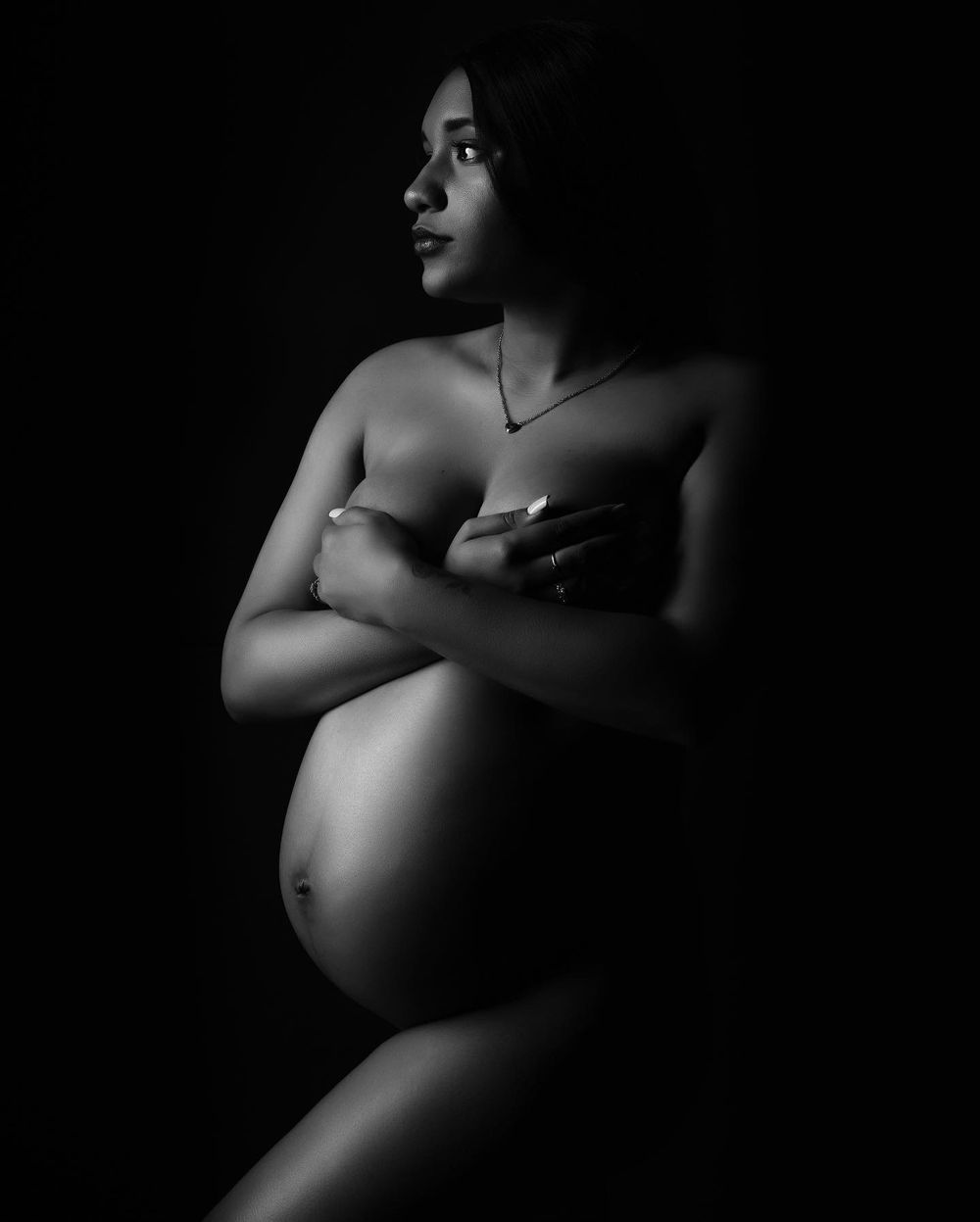 Low-key black and white maternity photography with dramatic shadows.