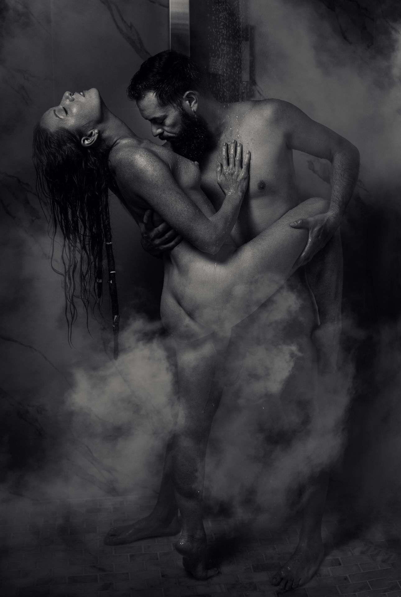 Artistic black and white photo of an intimate couple embracing in atmospheric fog.