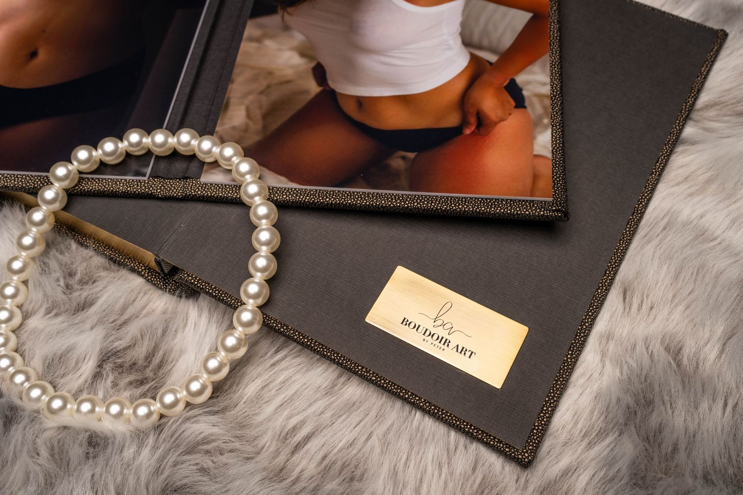 Pearl bracelet and leather wallet displayed on gray fur with photo frame in background.