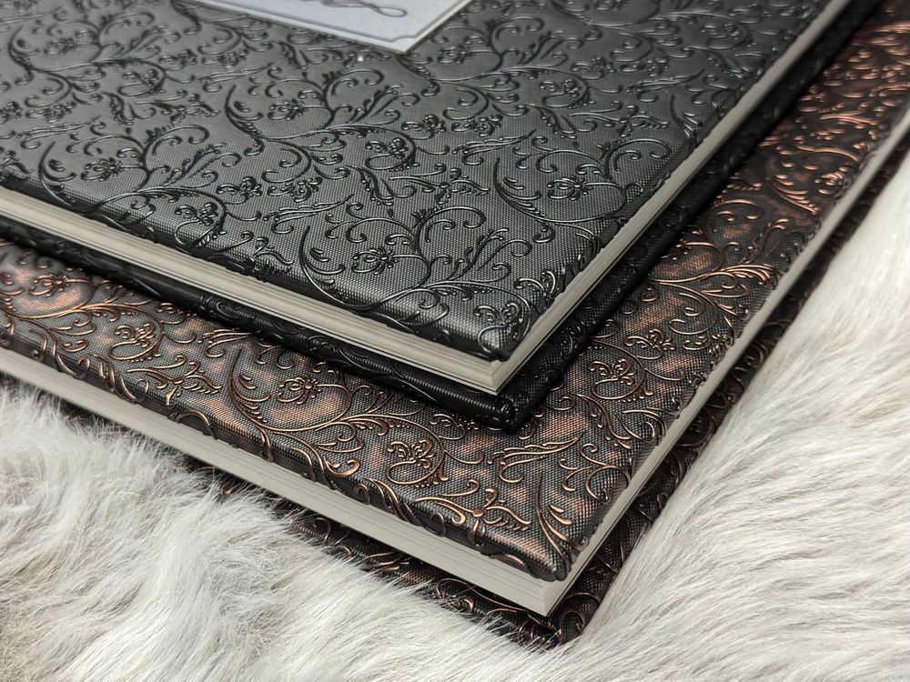 Leather-bound books with ornate embossed covers displayed on a white fur surface.