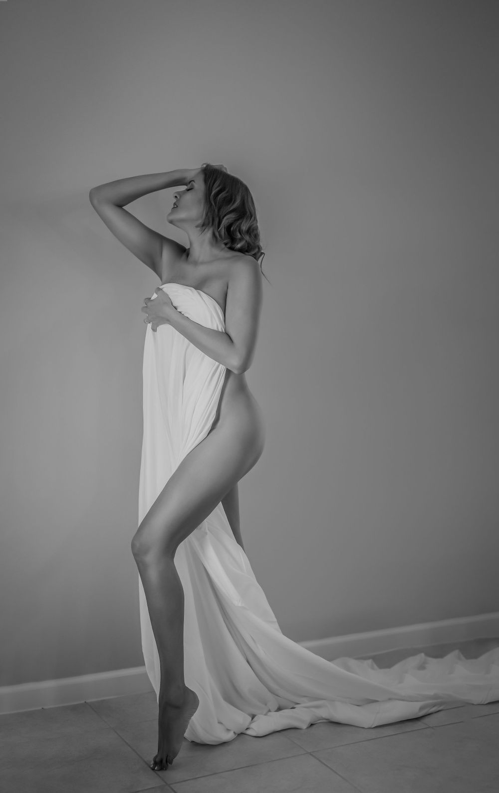 Artistic black and white photo of a figure draped in flowing white fabric against plain background.