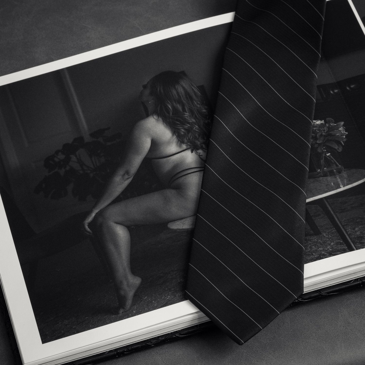 Open photography book displaying black and white boudoir portrait of a woman, with a striped tie resting on the page.